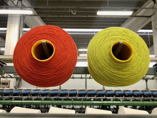 Bobine di filato arancione e giallo brillante montate su macchinari tessili industriali in un ambiente di fabbrica.