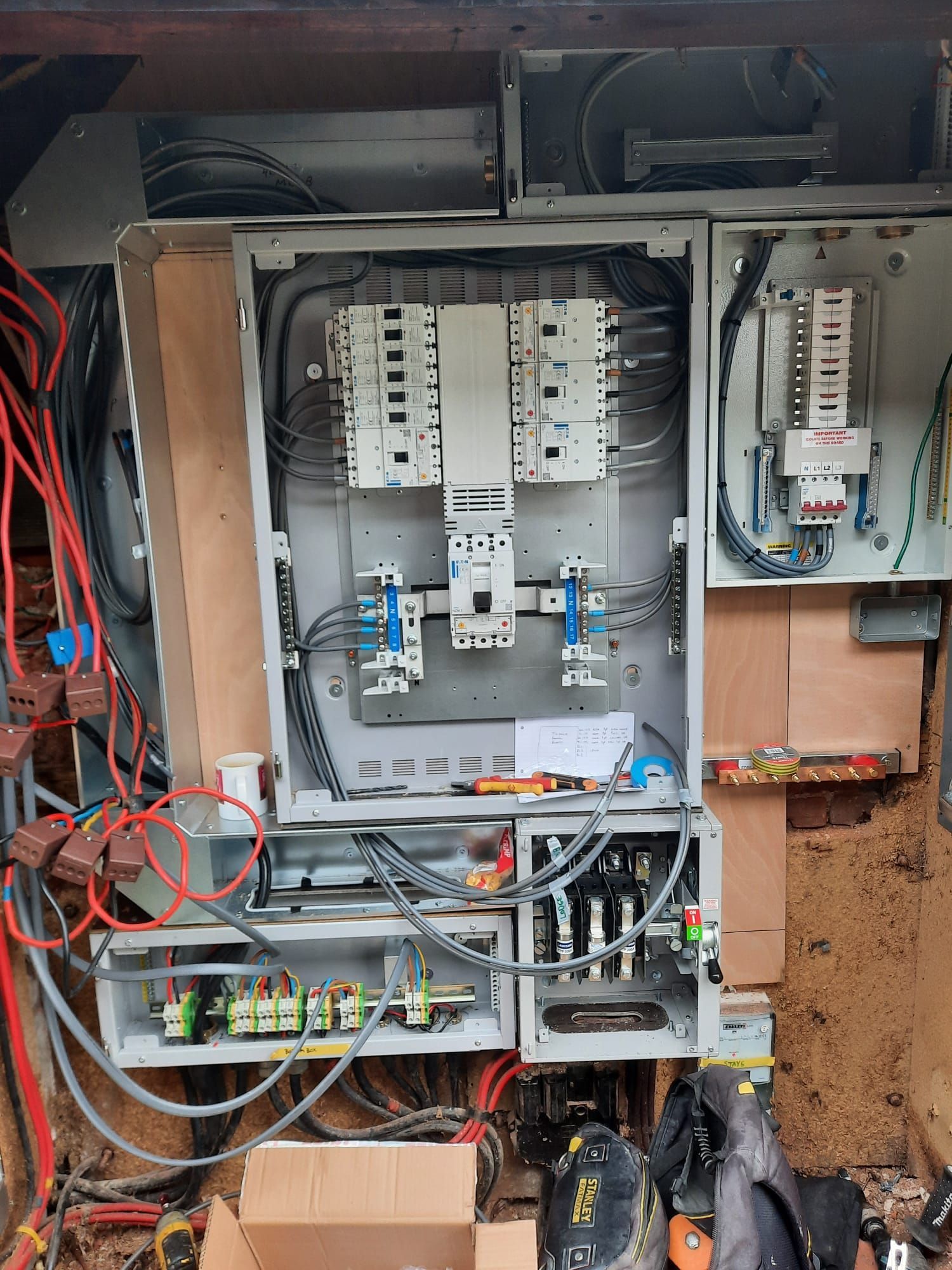 Electrical panel with numerous wires and circuit breakers, installed on a wooden surface.