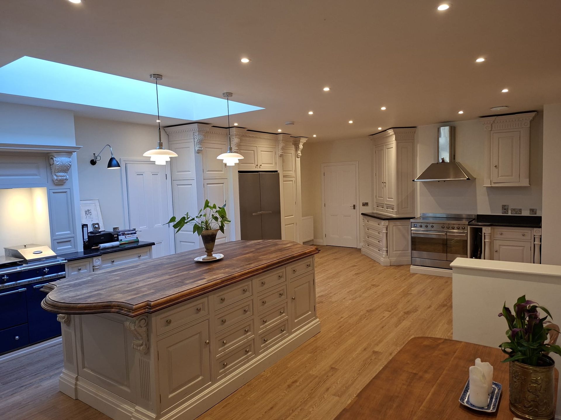 Bright modern kitchen with large island, wood floors, white cabinets, and stainless steel appliances