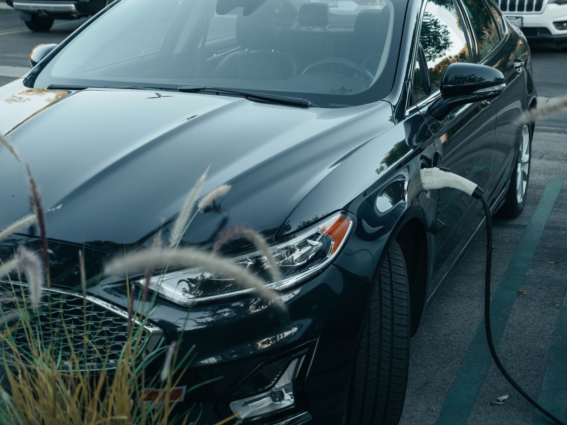 Black car parked, charging at a station. A charging cable is plugged into the car's side.
