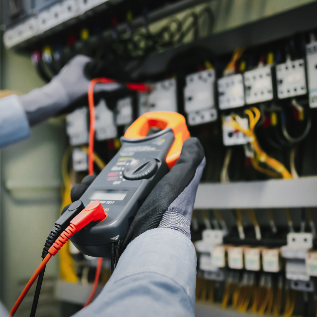 Electrician using a multimeter to inspect electrical panel wiring.