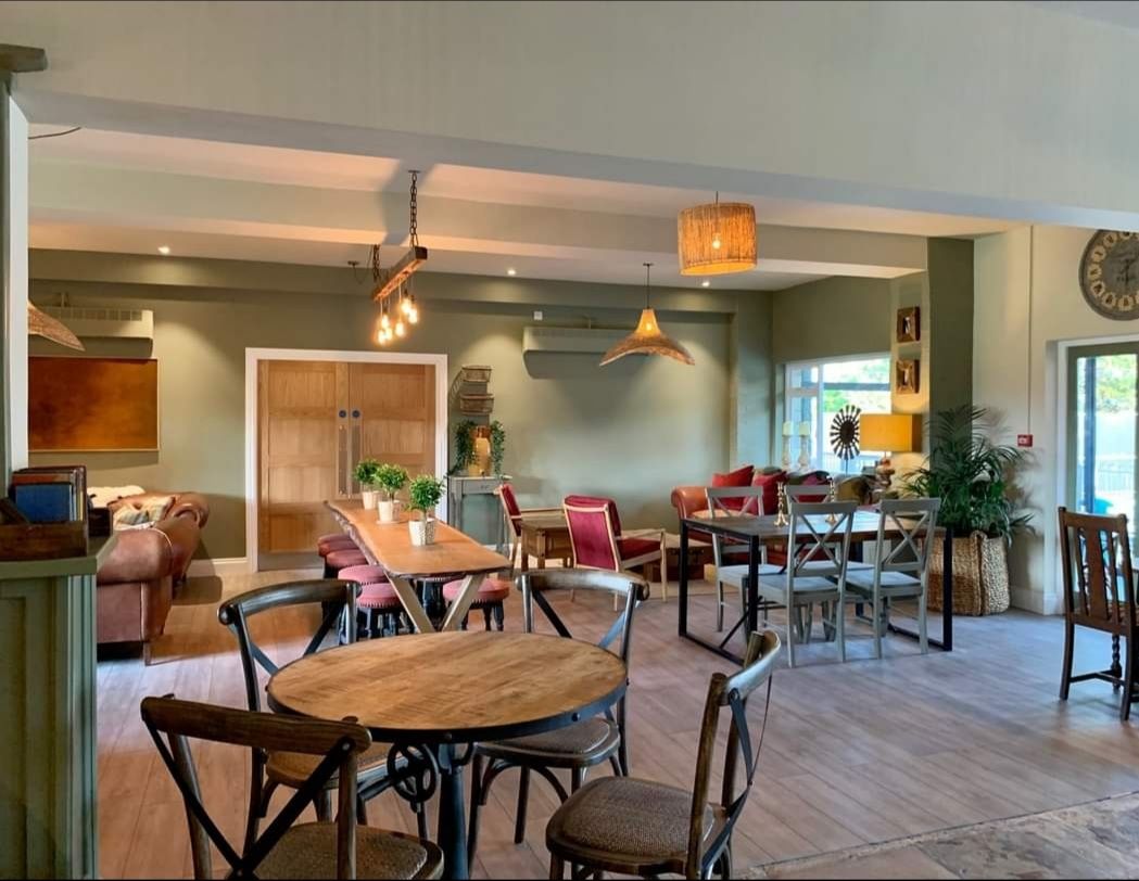 Interior of a cafe with wooden tables, chairs, and couches. Pale green walls and hanging lights.
