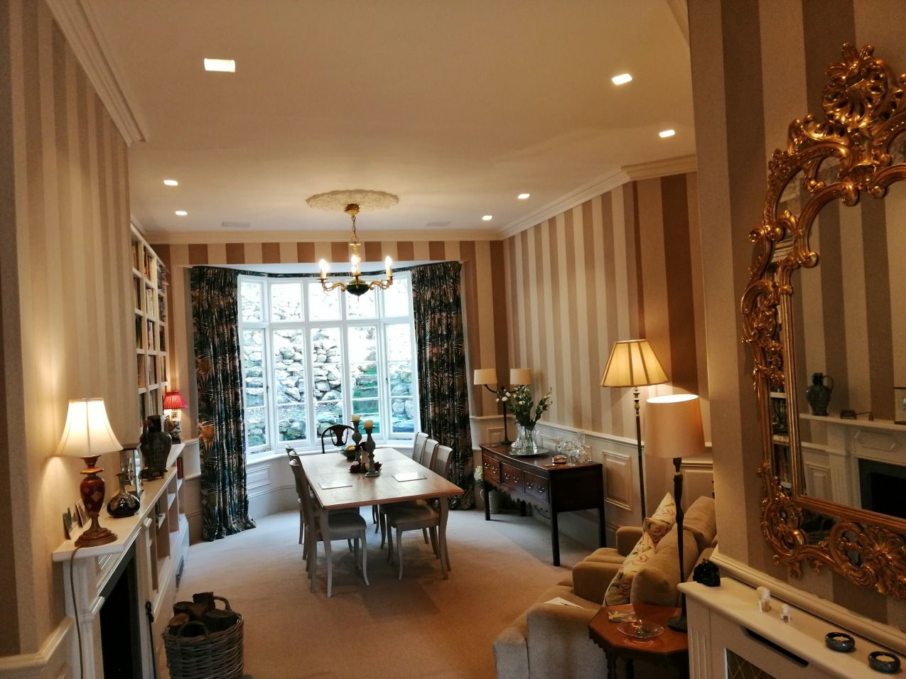 Dining room with striped wallpaper, dining table, chandelier, and a large ornate mirror.