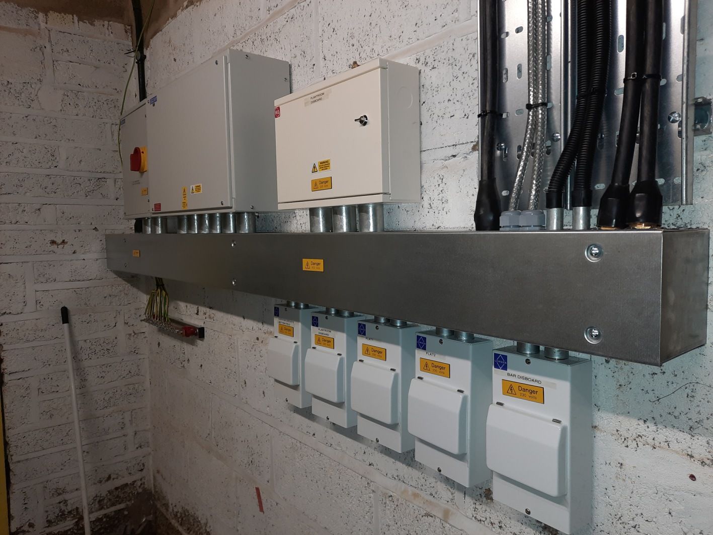 Electrical panel installation on a brick wall, with several white boxes and conduit pipes.