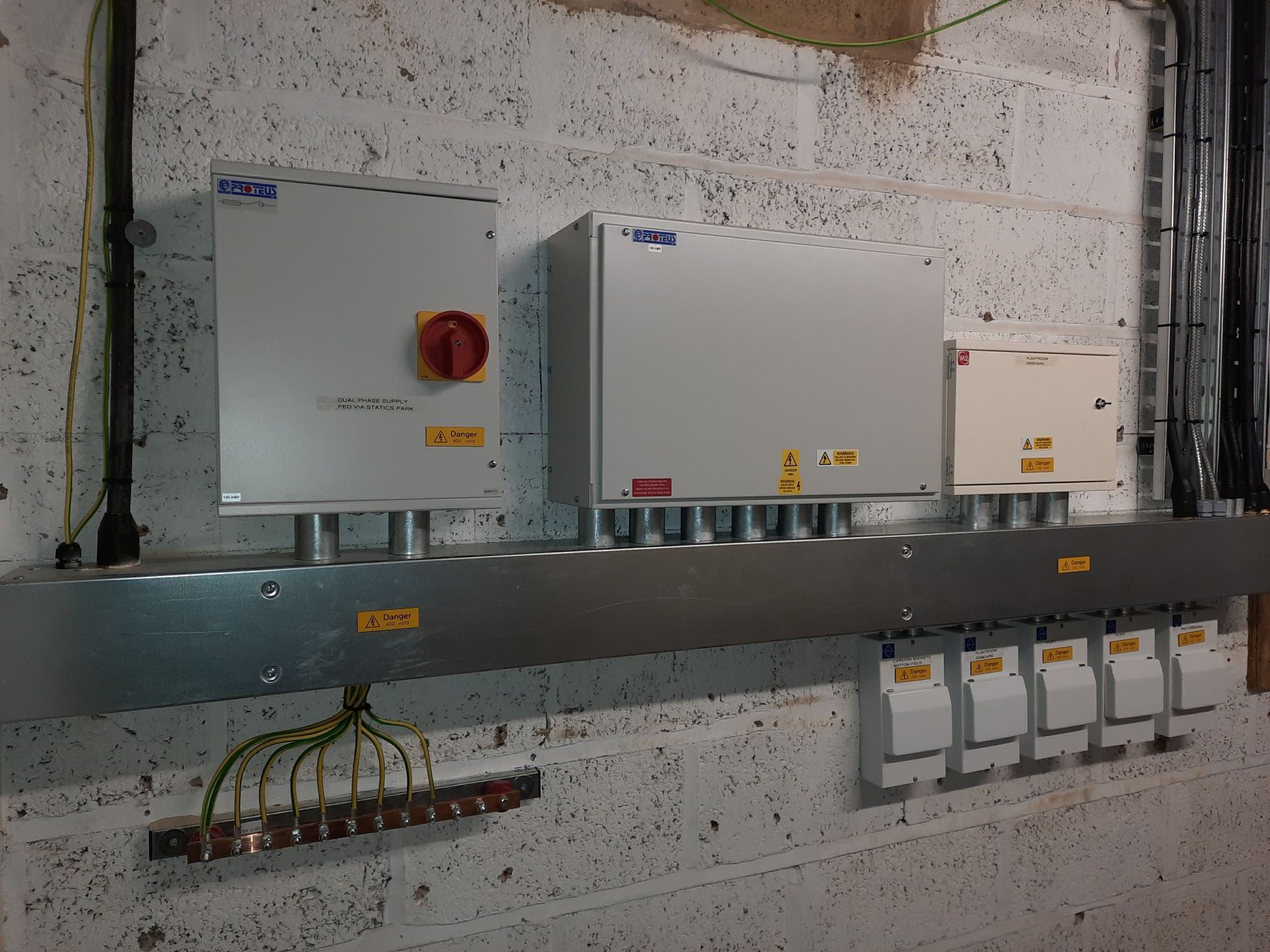 Electrical boxes and conduit mounted on a brick wall, including a switch, distribution units, and ground bar.