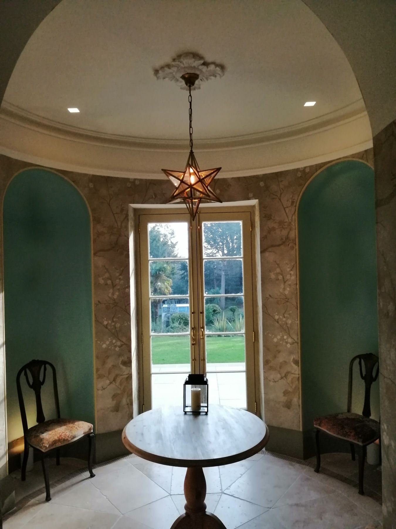 Round room with arched teal niches, round table, star pendant light, and chairs facing a door to a yard.