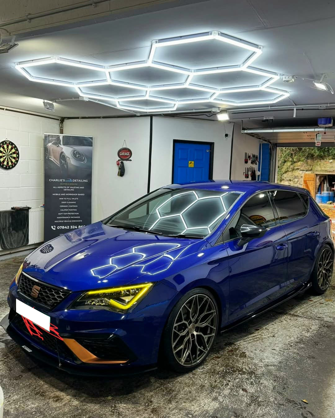 Blue Seat Leon car parked under hexagon-shaped LED lights in a garage.
