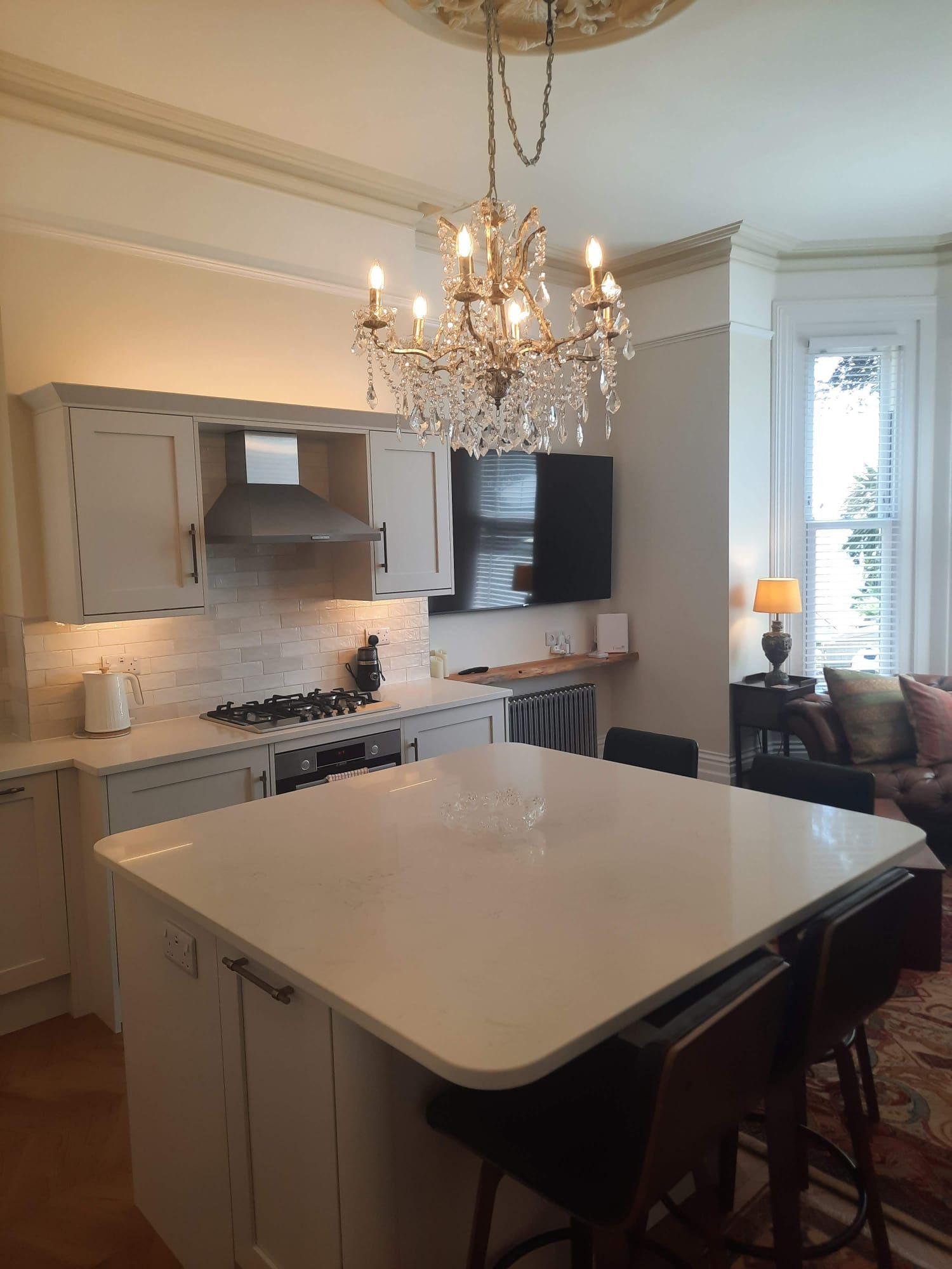 Kitchen with island, chandelier, stovetop, and mounted TV. Light cabinetry and white countertops.
