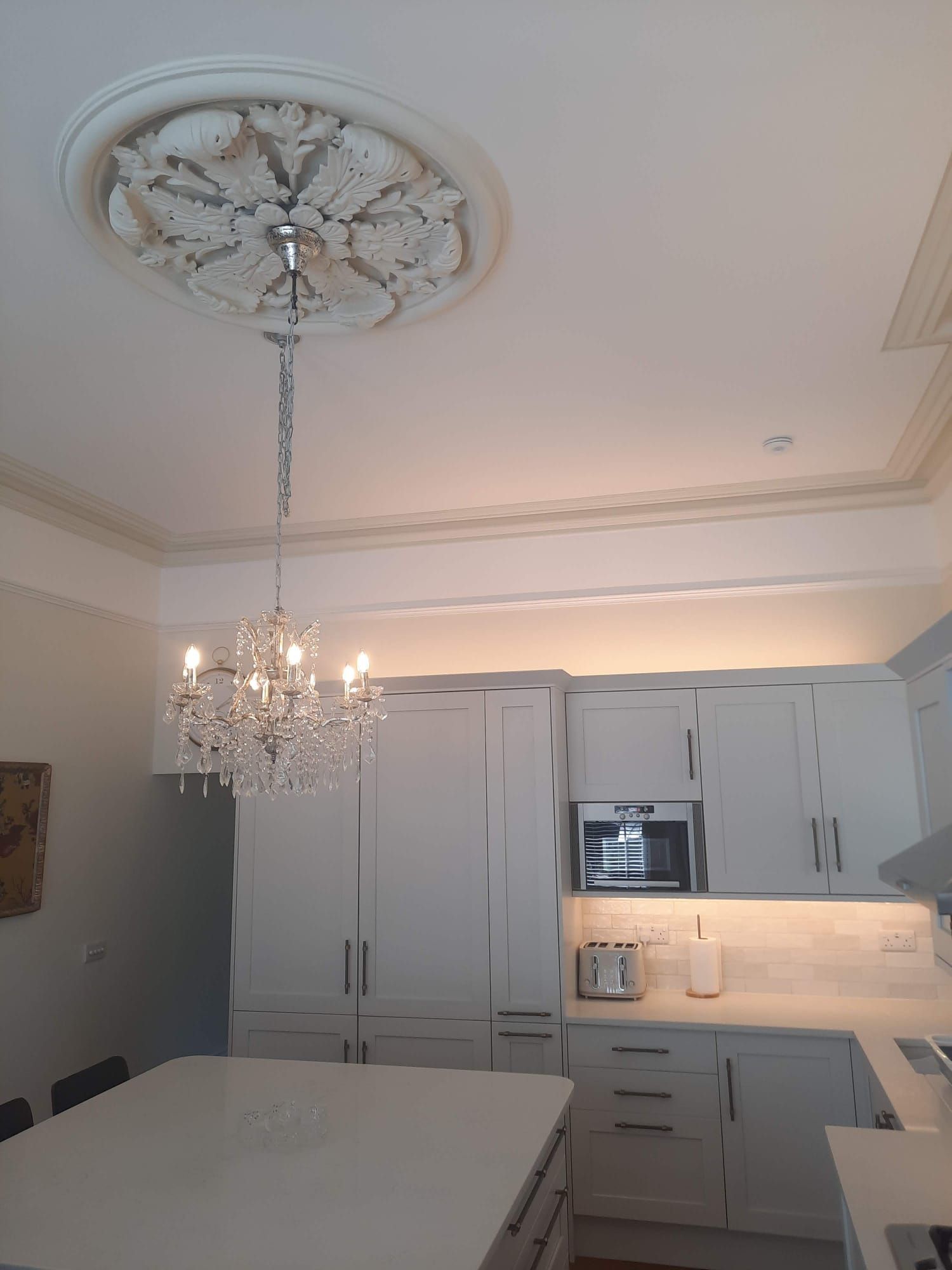 Kitchen with white cabinets, island, and crystal chandelier hanging from a decorative ceiling medallion.