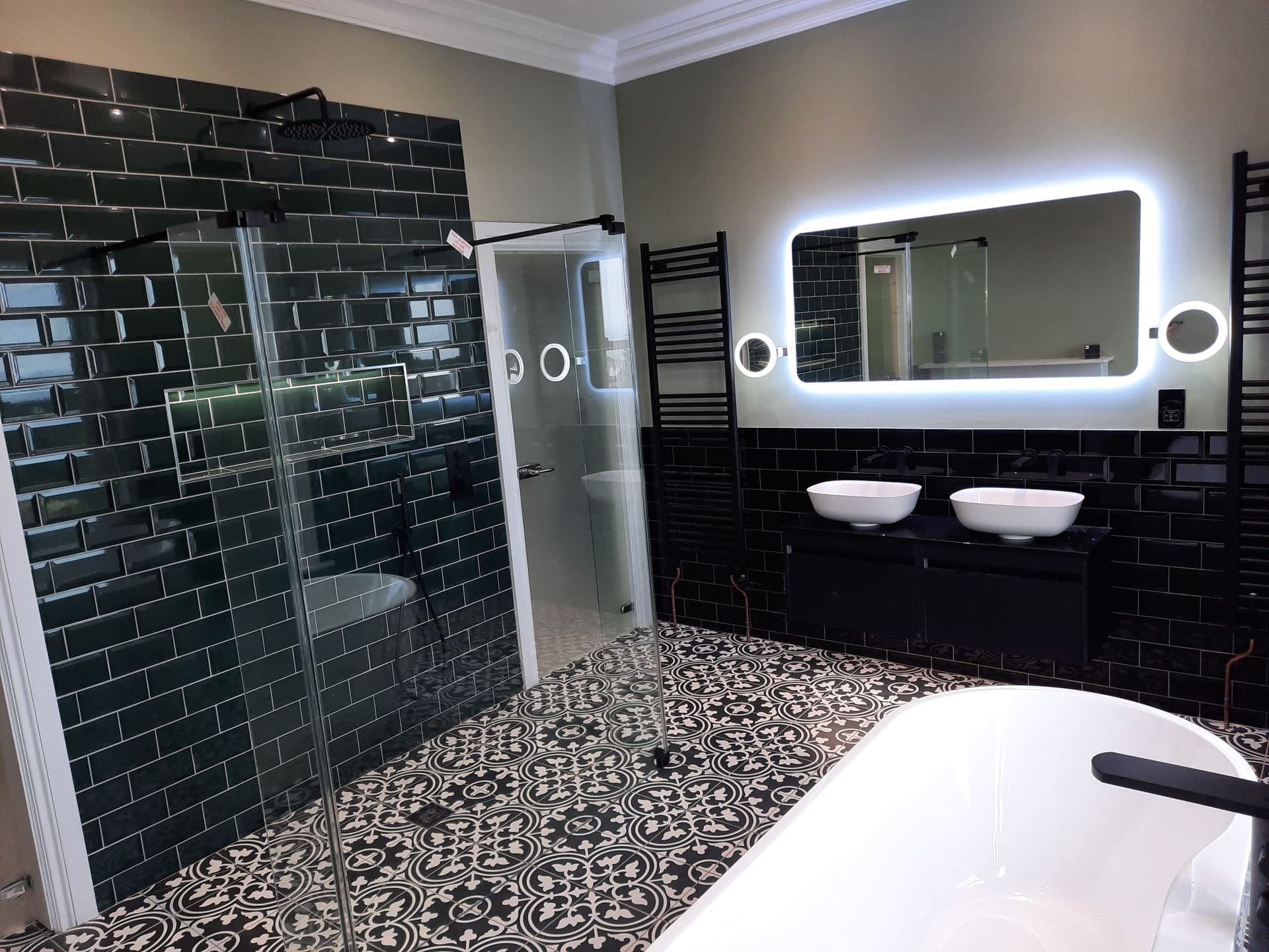 Modern bathroom with black tiled walls, a glass shower, patterned floor, and a white soaking tub.