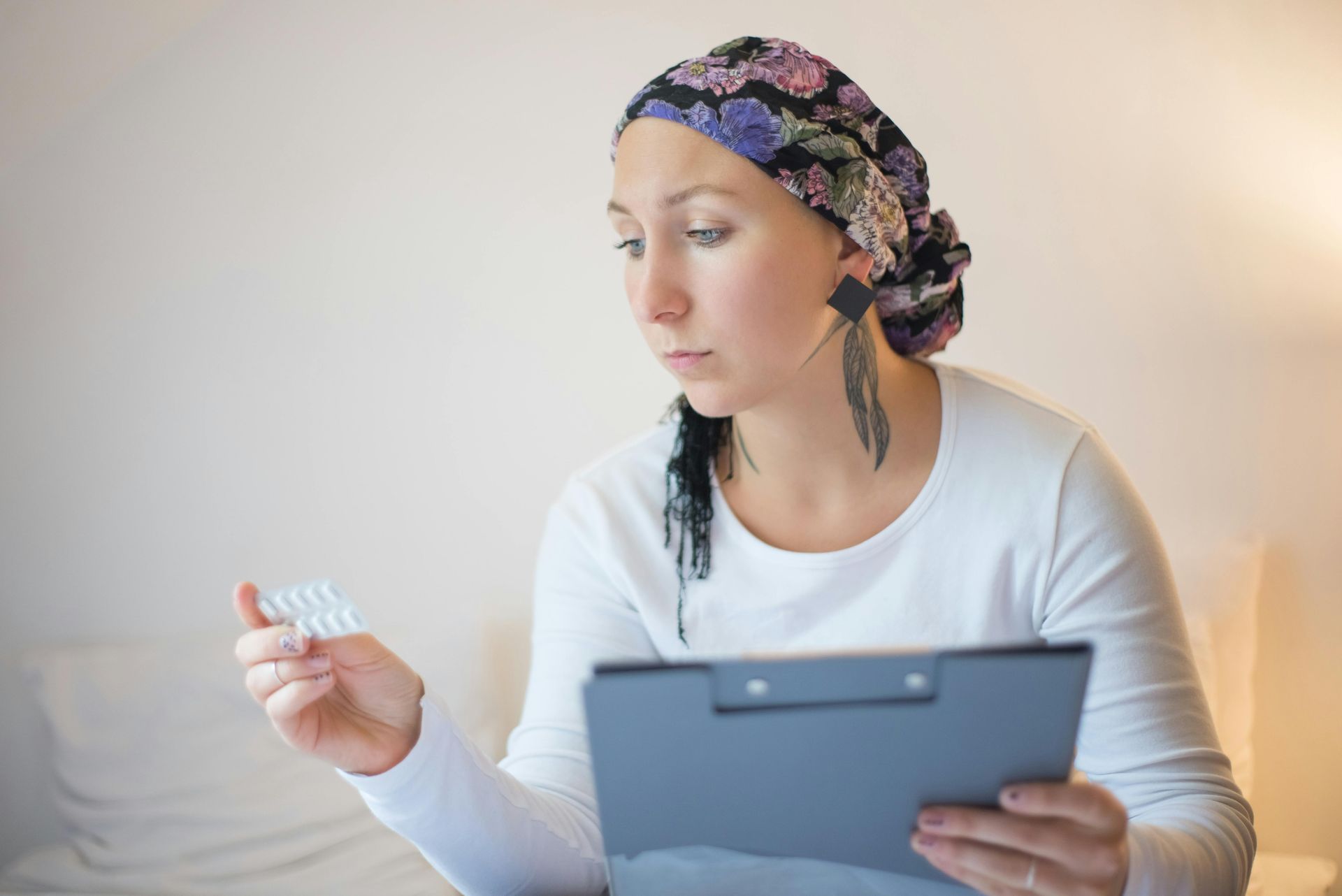 Woman holding a tablet and a small pill bottle, looking at a tablet screen in a bright room.