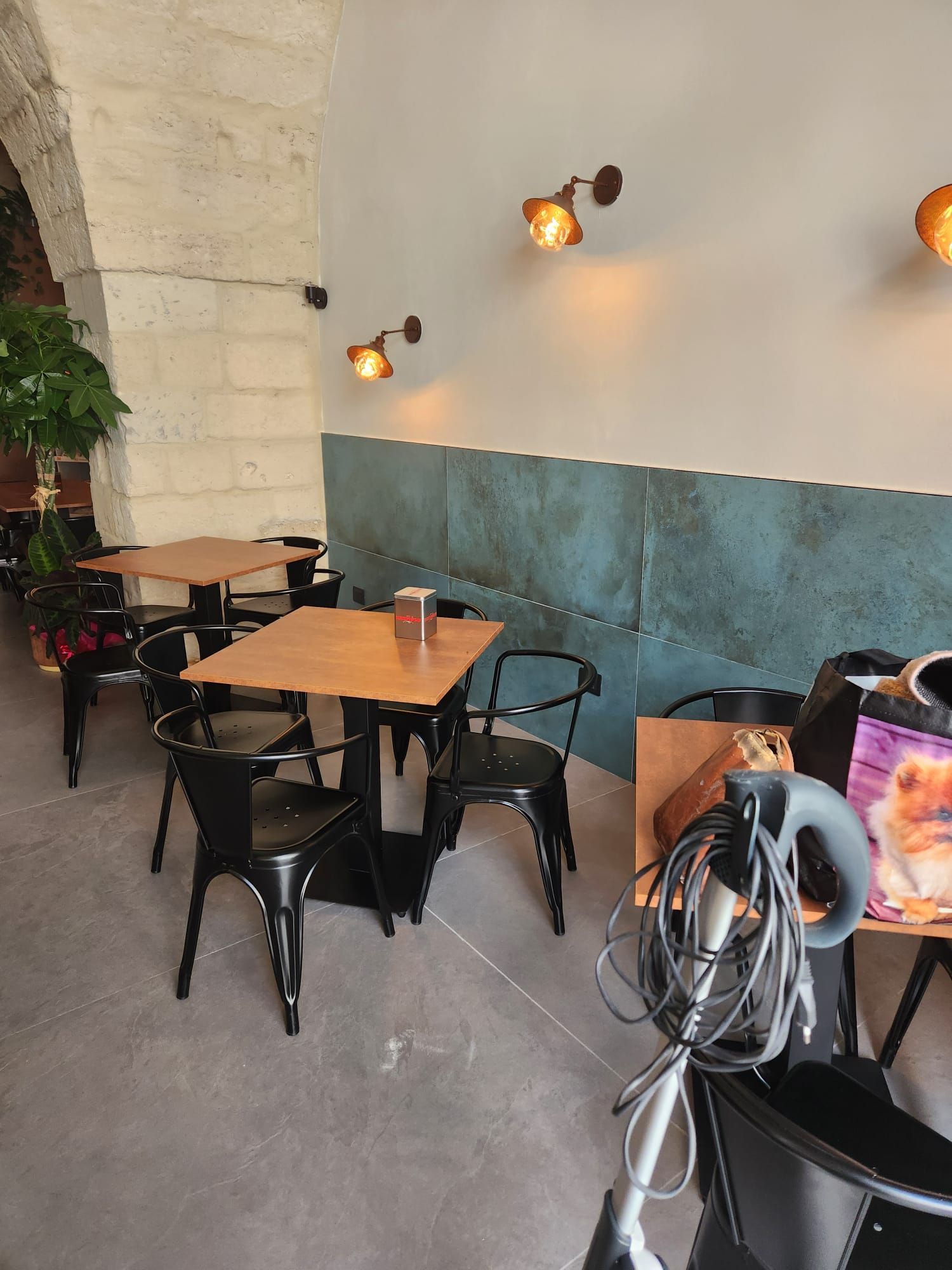 Piccola area con tavolini da caffè, sedie nere, applique e attrezzi per la pulizia in un angolo.