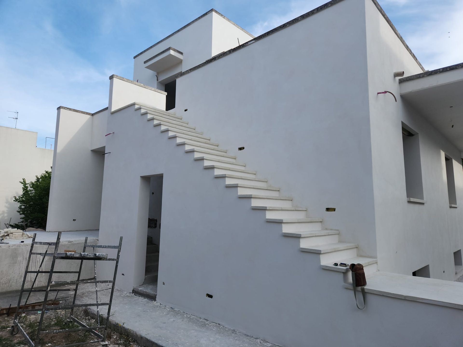 Edificio moderno bianco con scala esterna e terrazza sul tetto sotto un cielo azzurro.
