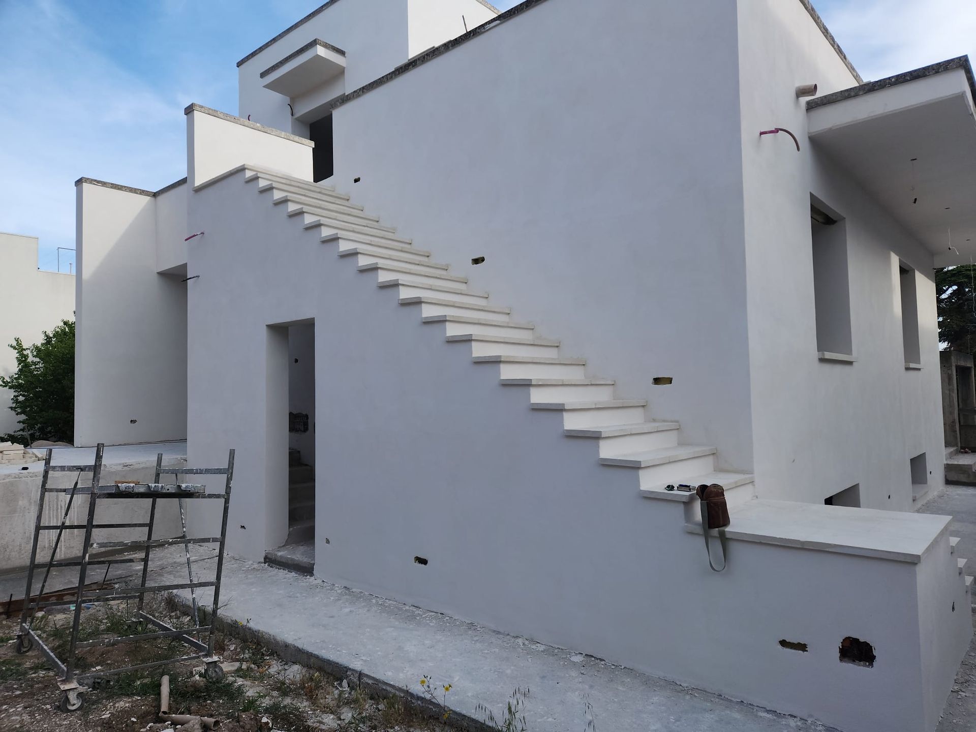 Esterno di una casa bianca con una scala in cemento grezzo lungo la parete laterale.