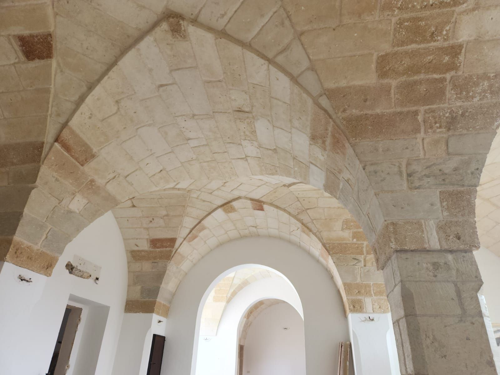 Archi a volta in pietra in un corridoio luminoso con pareti bianche e porte ad arco
