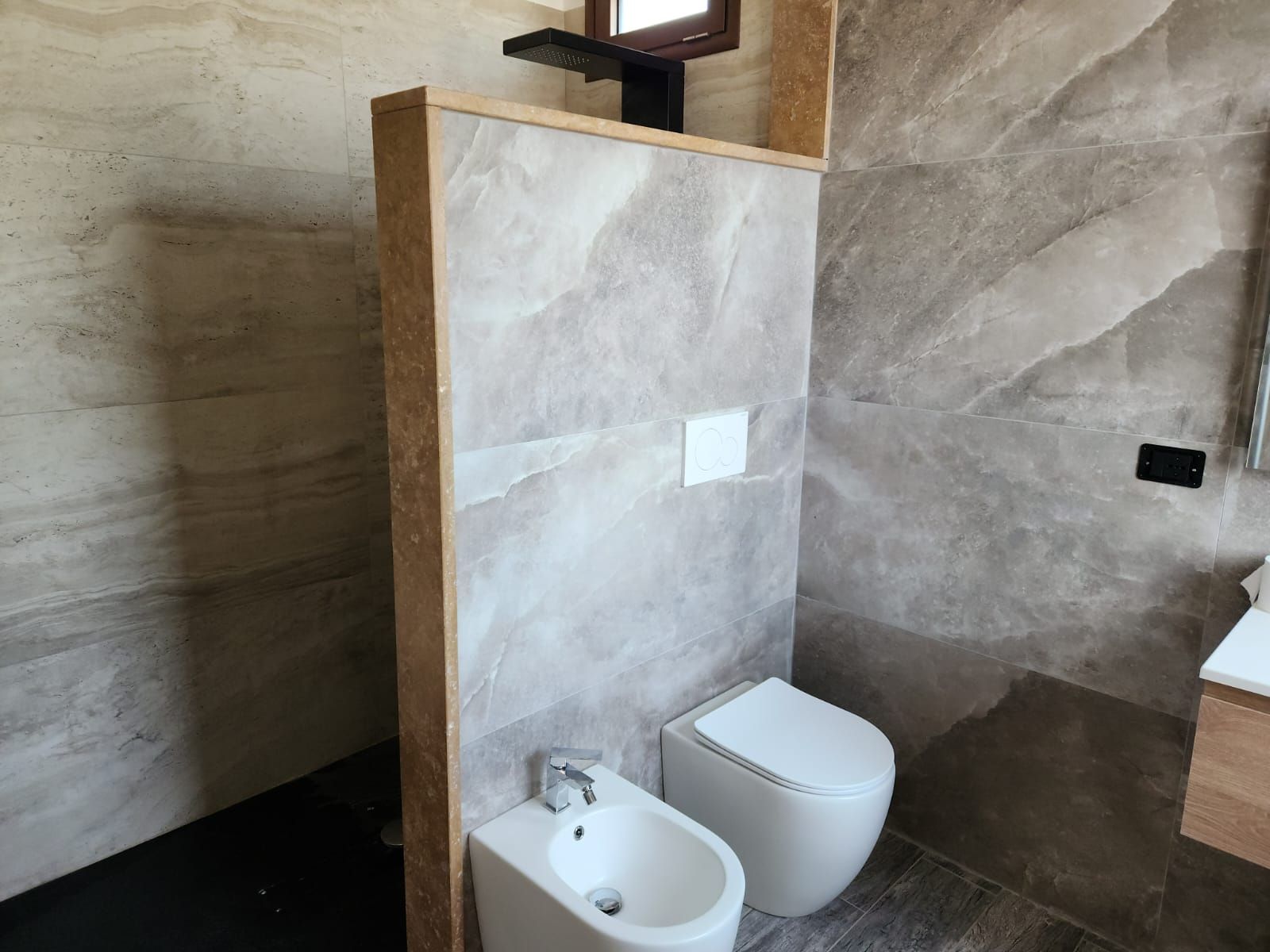 Bagno moderno con bidet, WC e pareti rivestite con piastrelle effetto pietra.