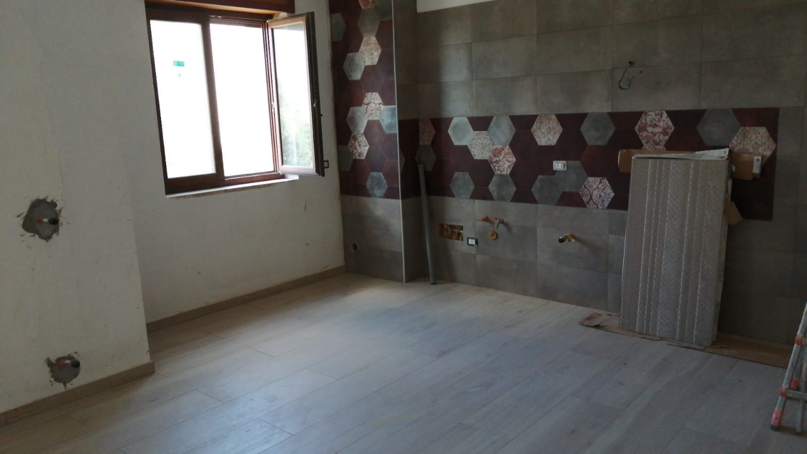 Stanza vuota con pavimento piastrellato, finestra e piastrelle decorative alle pareti, attualmente in fase di ristrutturazione.