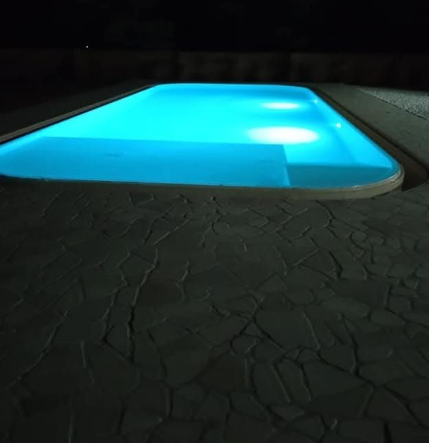 Una piscina notturna che brilla di un blu intenso accanto a un patio in pietra scura.