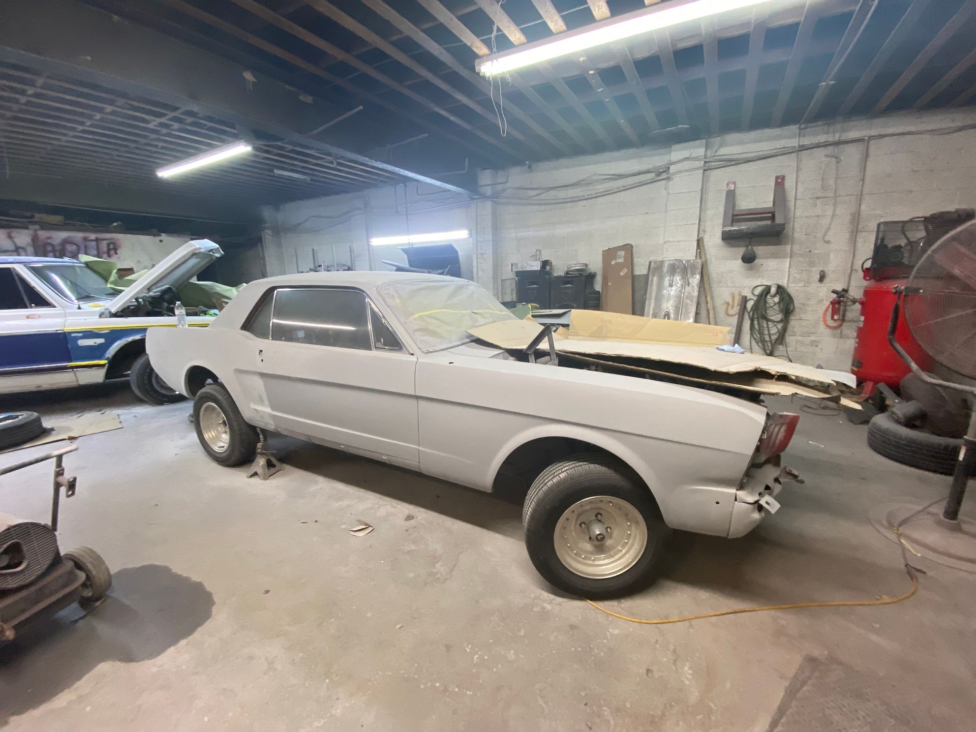 Silver classic car under repair in a garage, with the hood open and front missing.