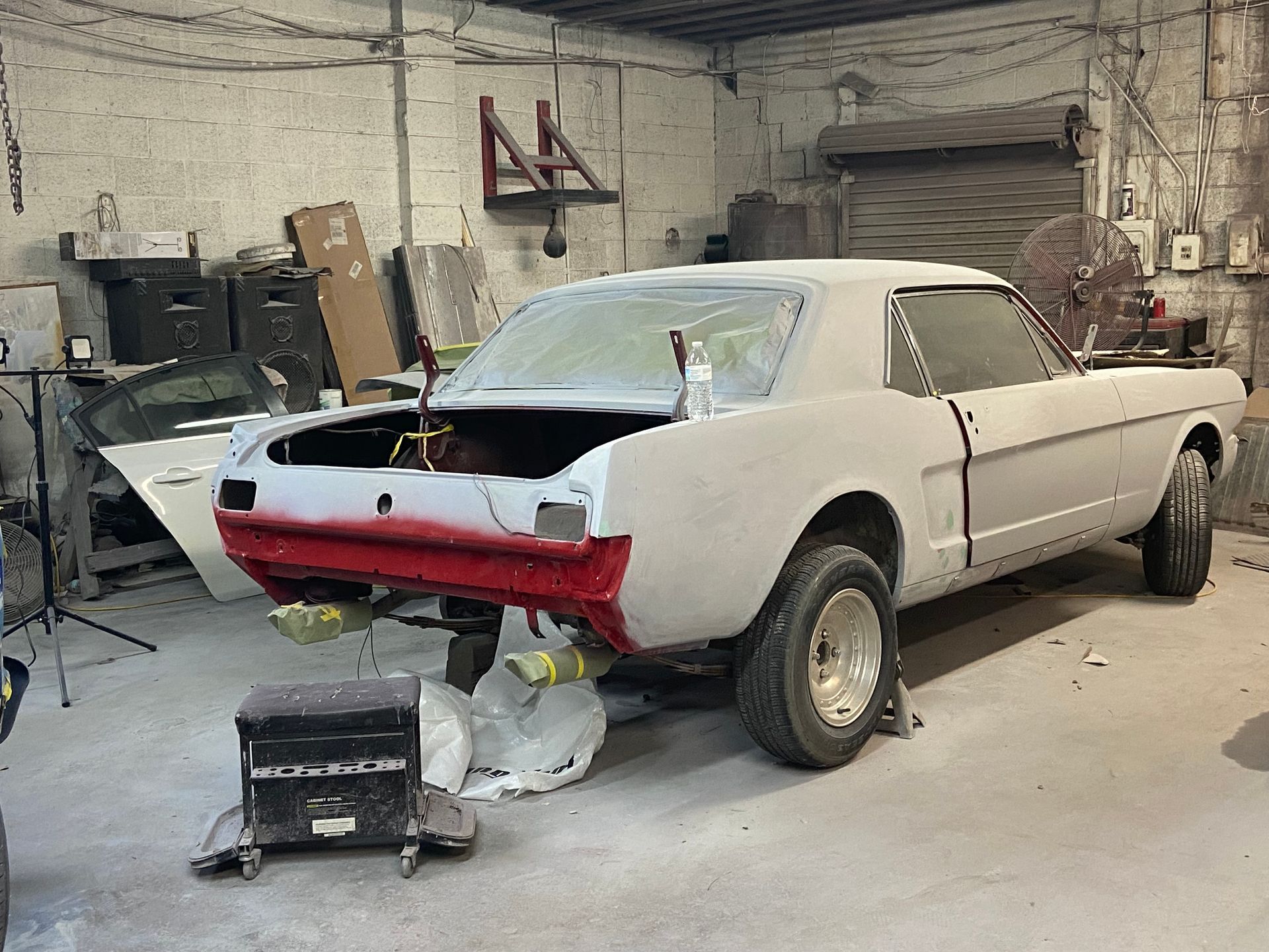 Partially restored red-and-white classic car in a workshop garage, with tools and parts nearby