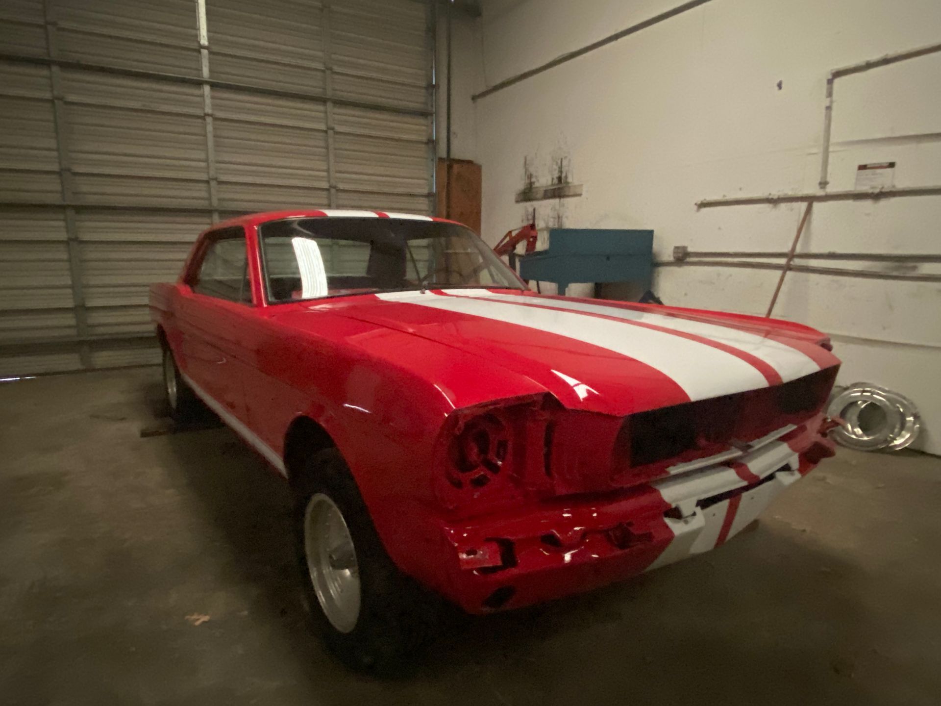 Red classic muscle car with white racing stripes parked in a garage