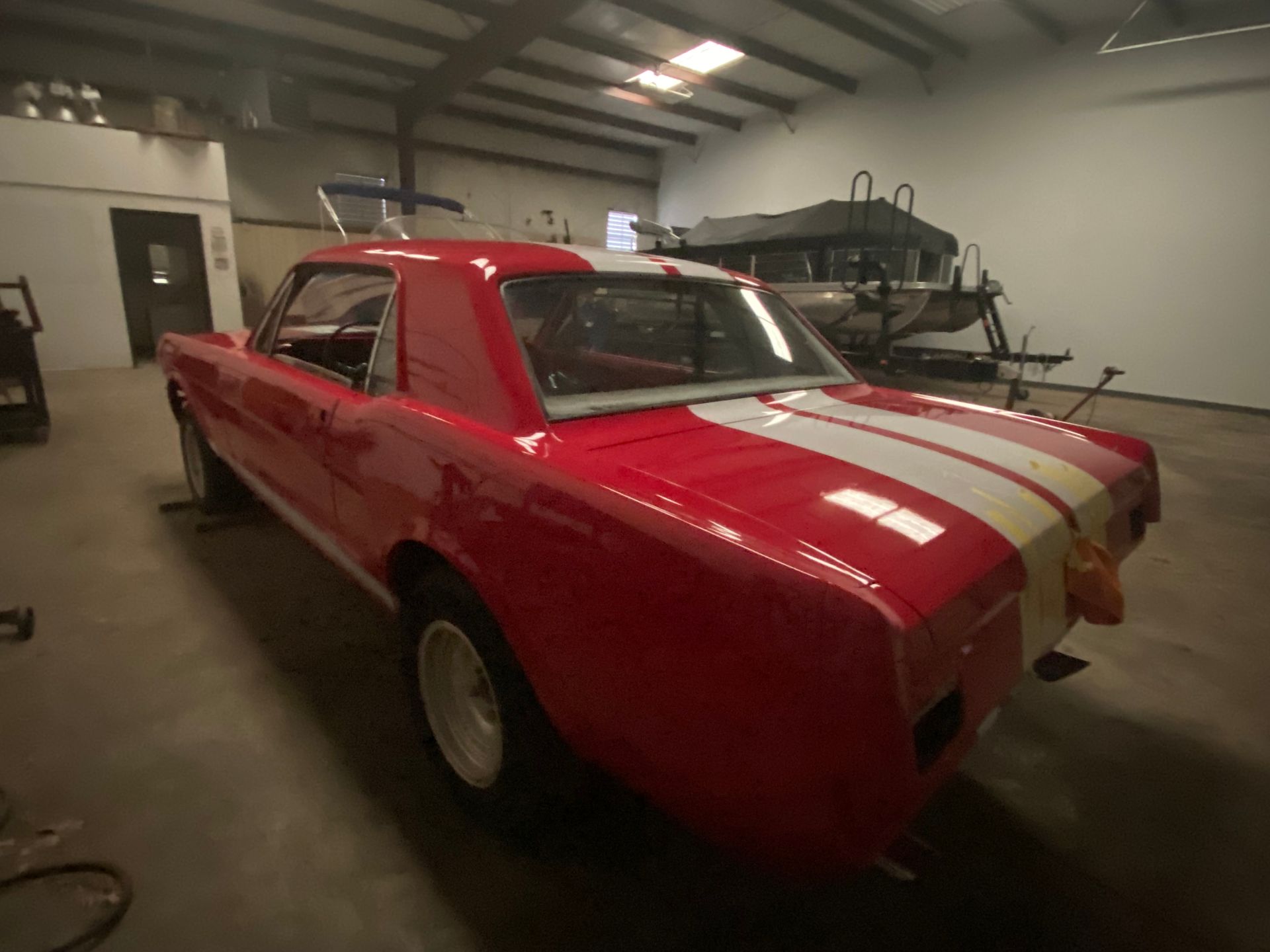 Red classic car with white racing stripes parked inside a garage or workshop.