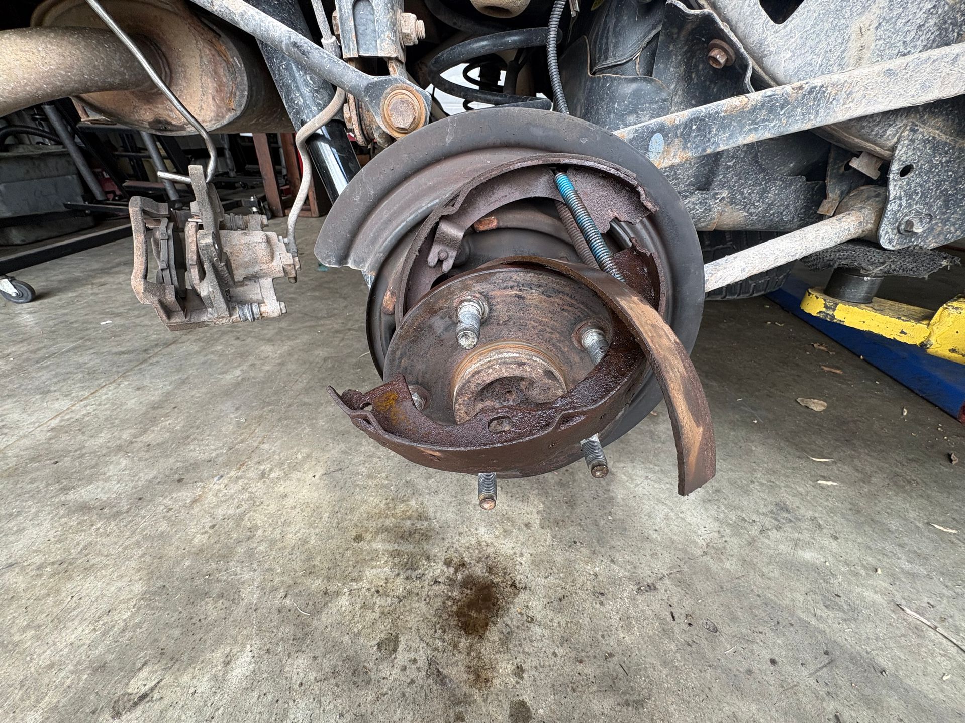 Rusty car brake rotor and suspension parts exposed with the wheel removed in a garage.