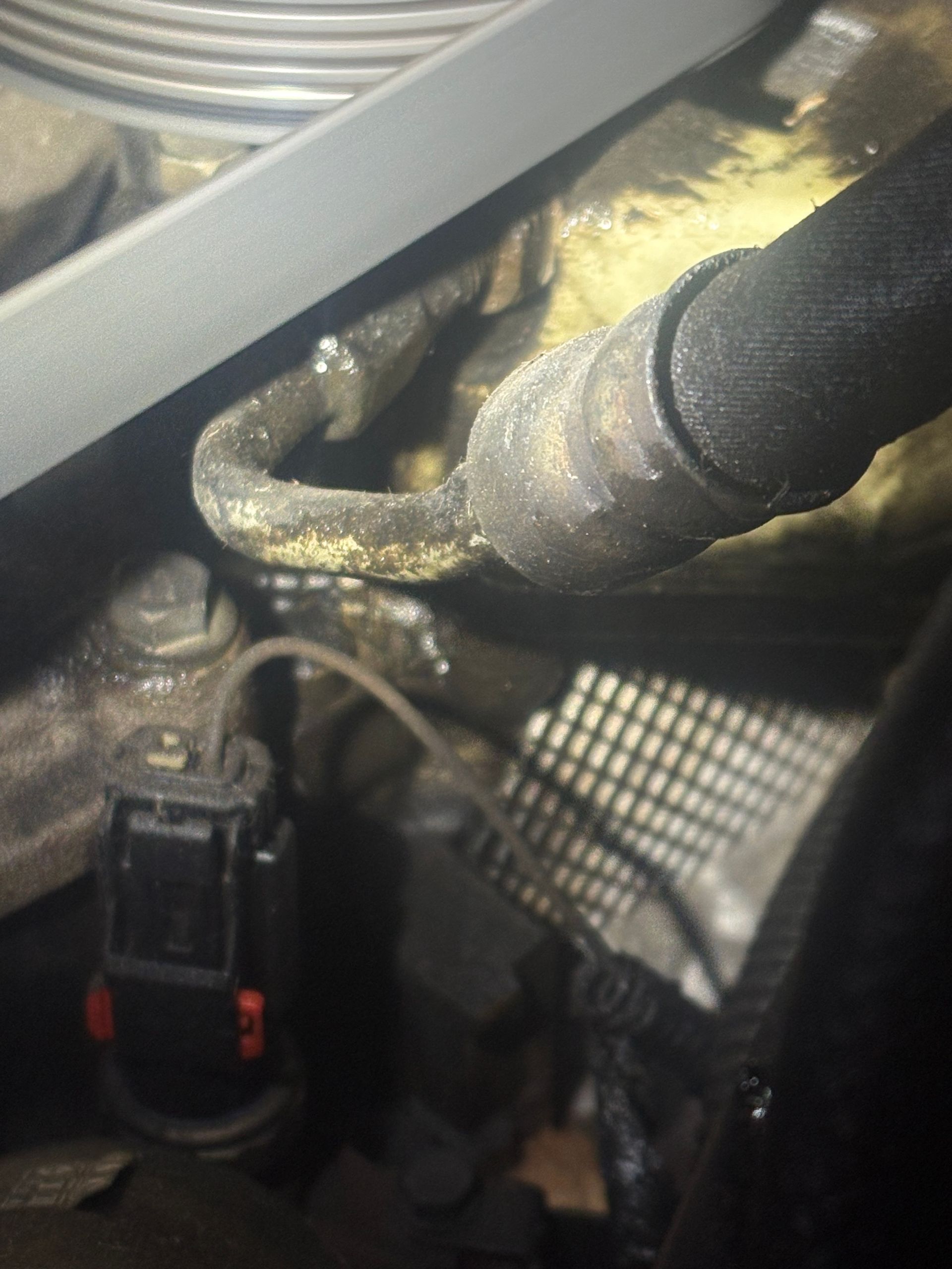 Close-up of a car engine hose connection wrapped in black insulation, with a connector below.
