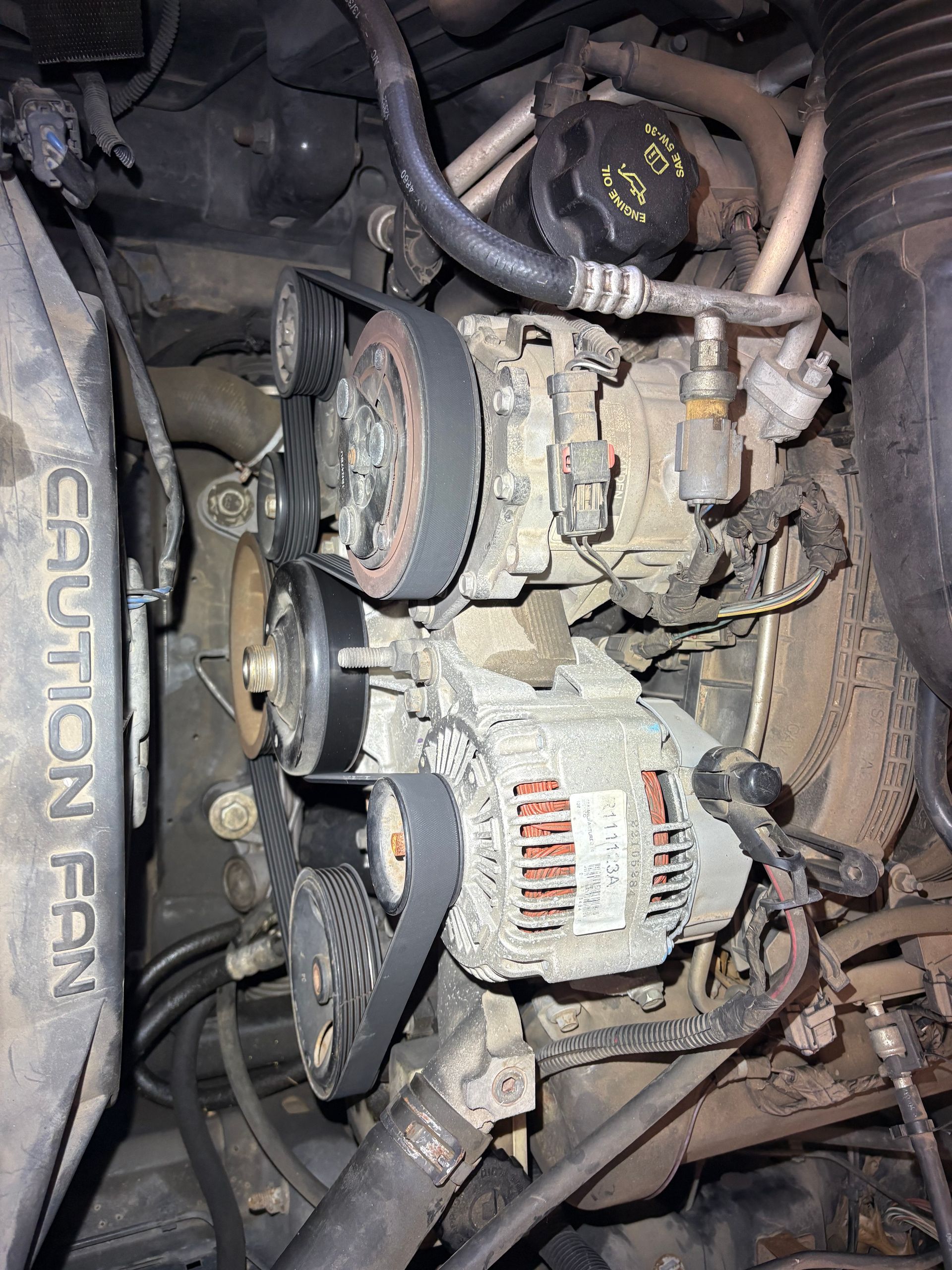 Dirty car engine with alternator, belts, and hoses under the hood