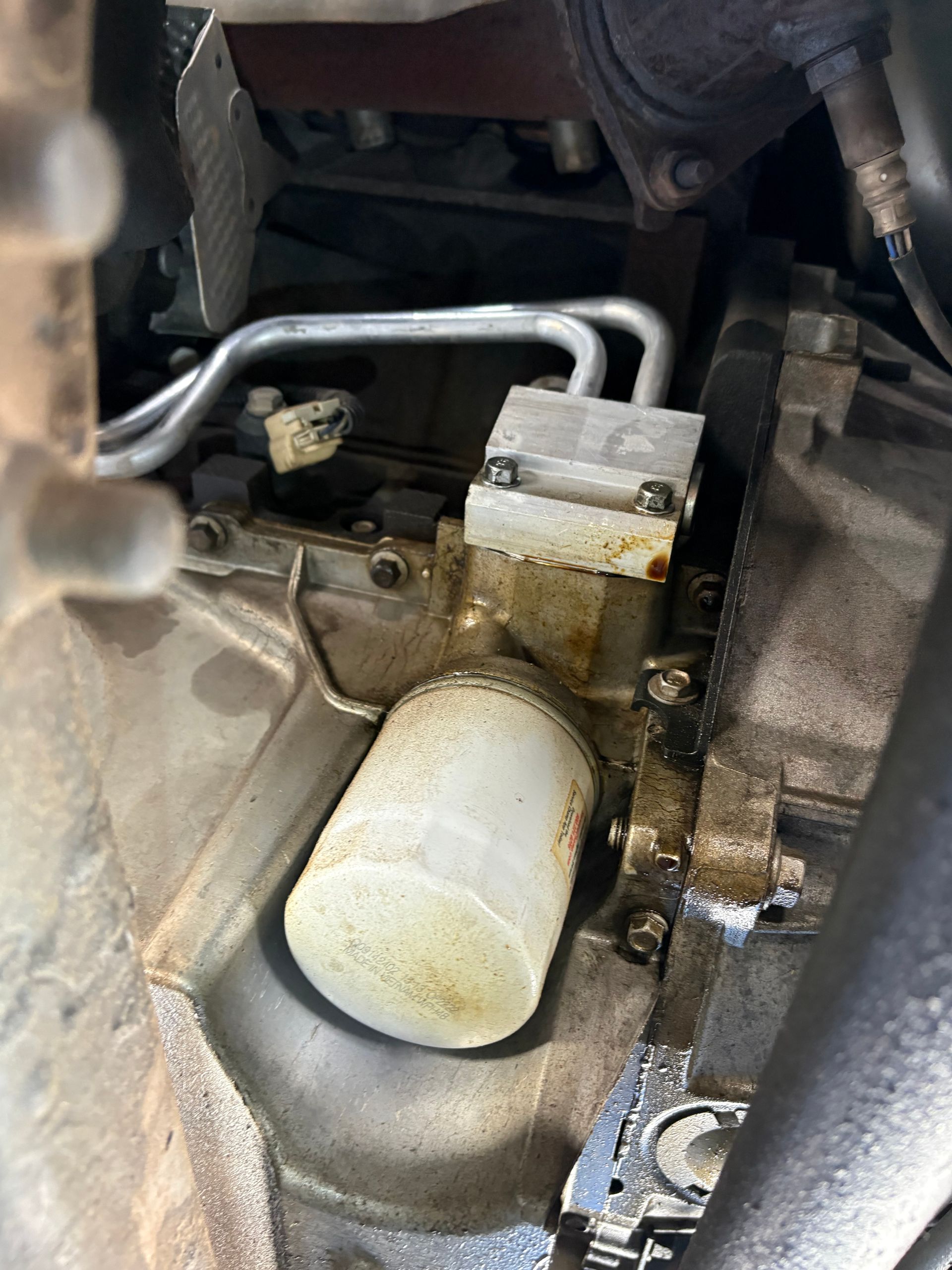 Close-up of a dirty engine component with a white cylindrical filter and metal tubing inside a mechanical housing
