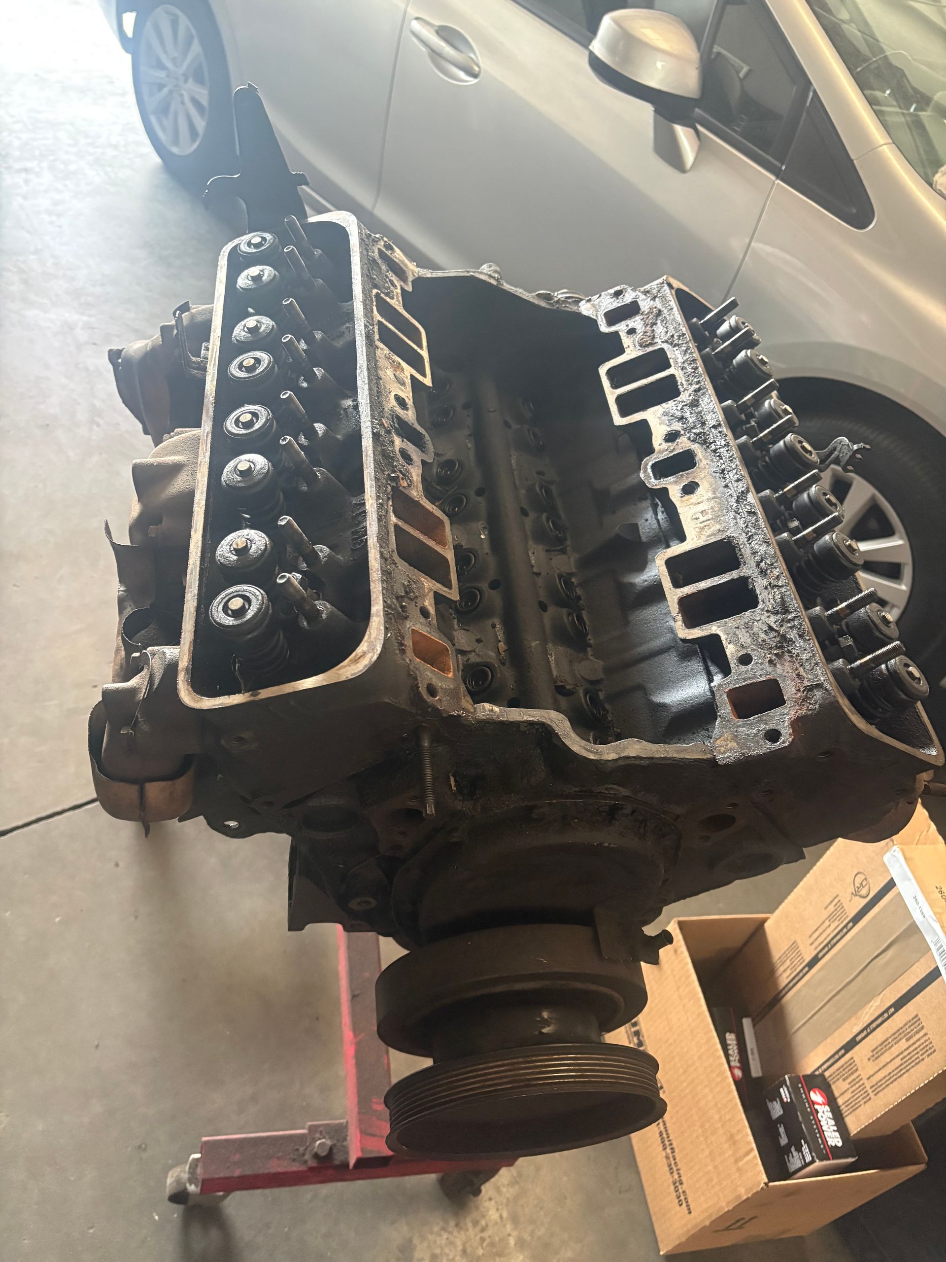 Car engine block on a floor jack in a garage, with a car parked beside it.