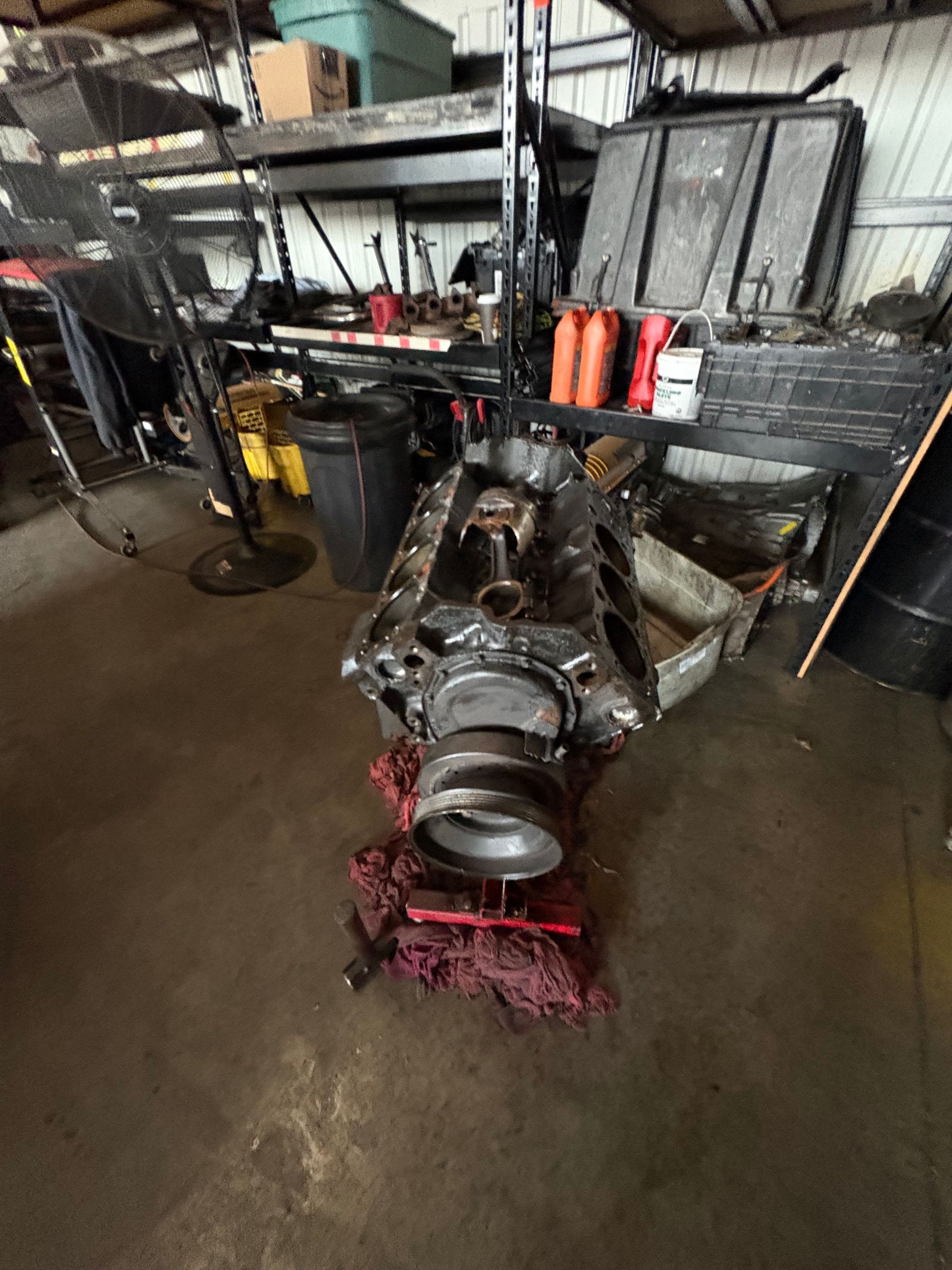 Car engine transmission assembly on a red jack in a cluttered auto shop garage