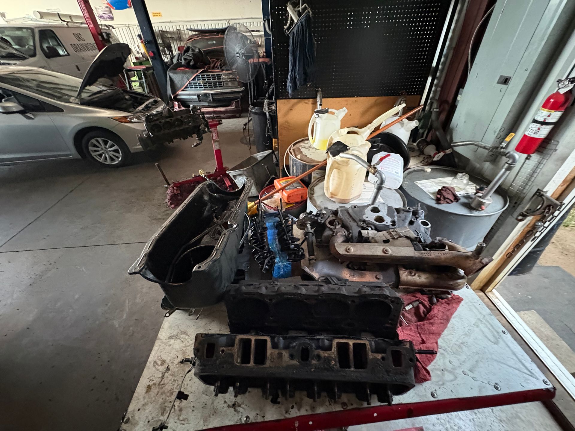 Engine on a garage floor with tools and a silver car in the background