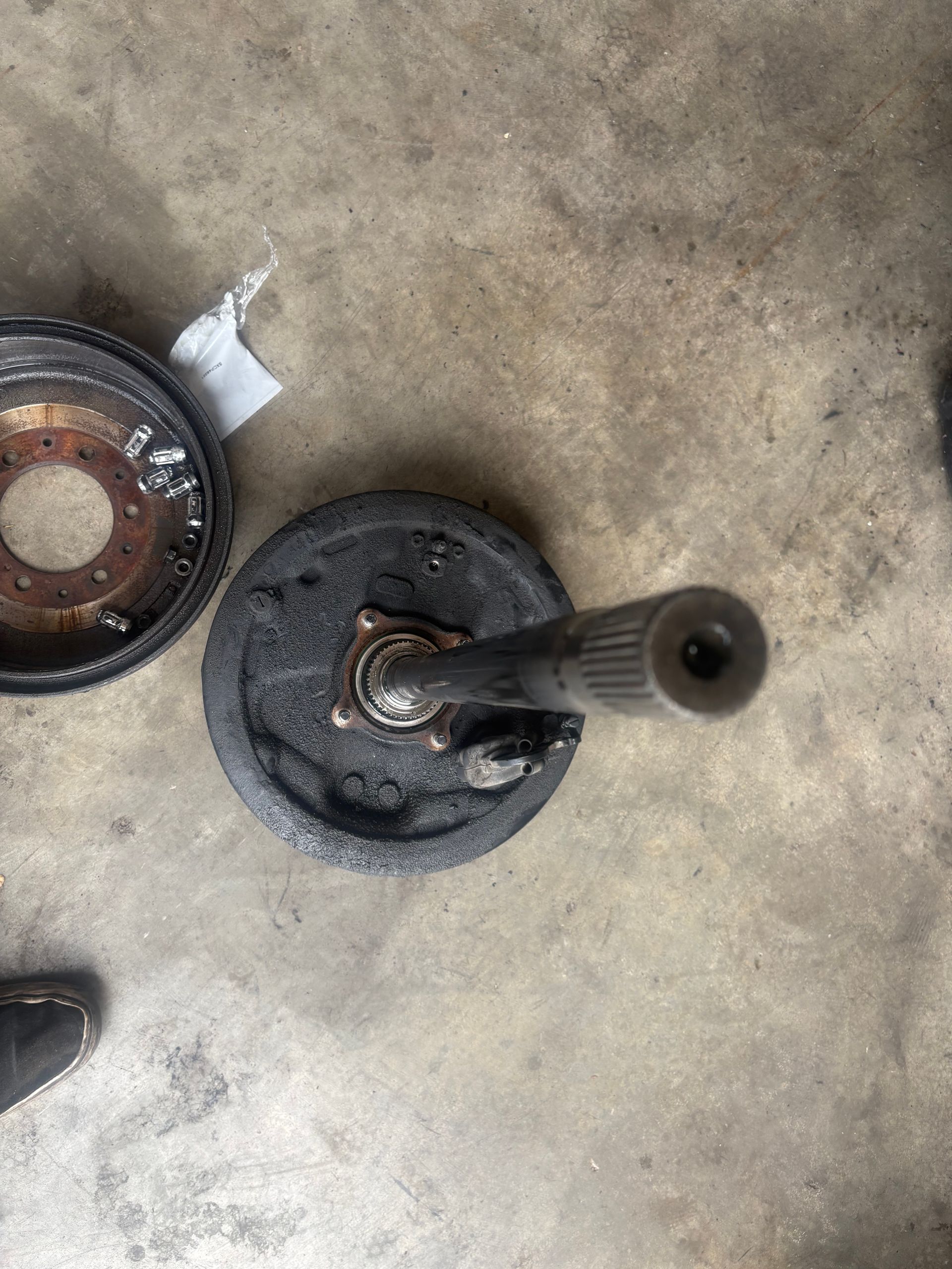 Two disassembled dark metal parts on a concrete floor, one with a protruding rod.