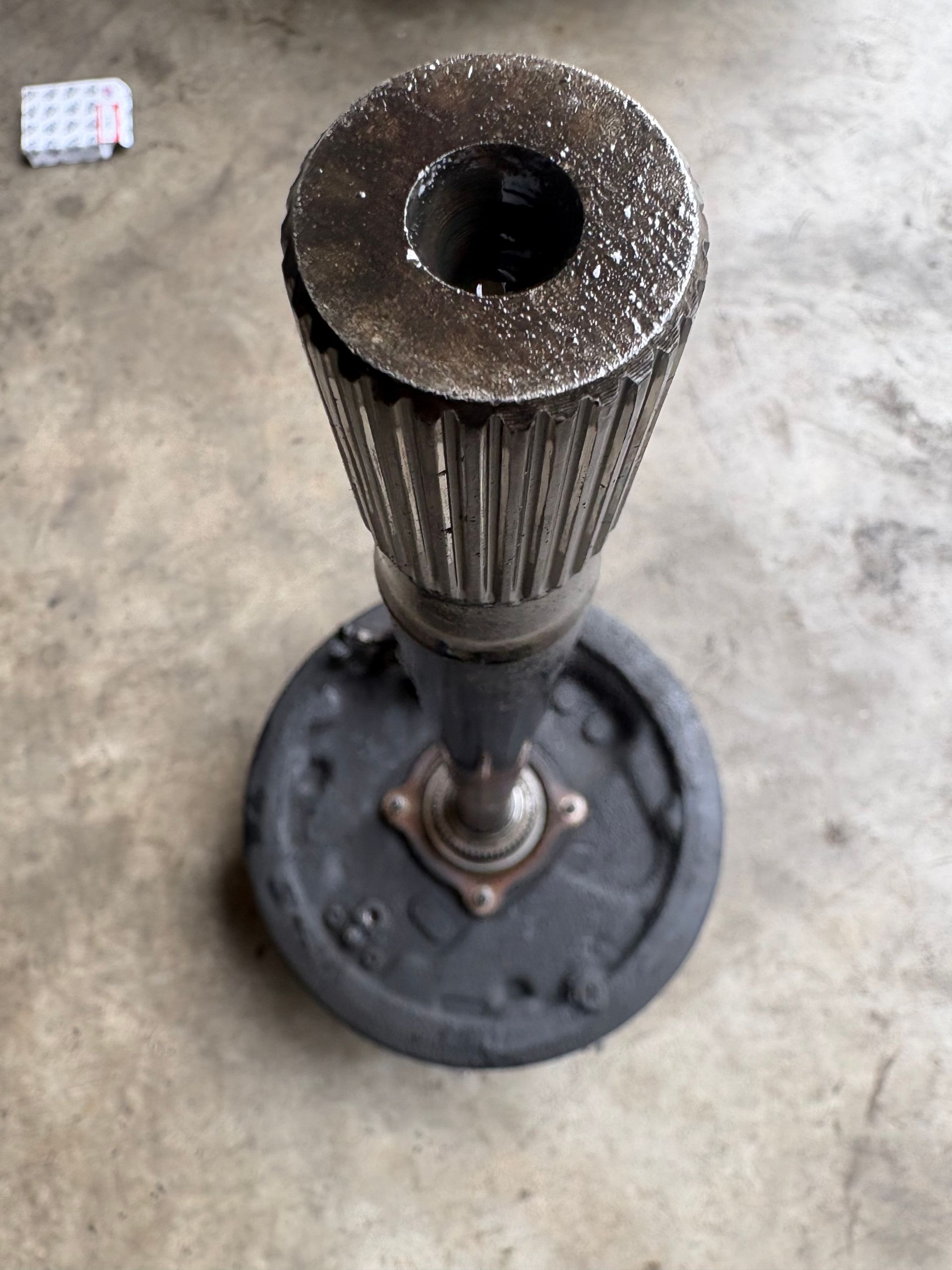 Rusty metal pedestal with a round base on a concrete floor.