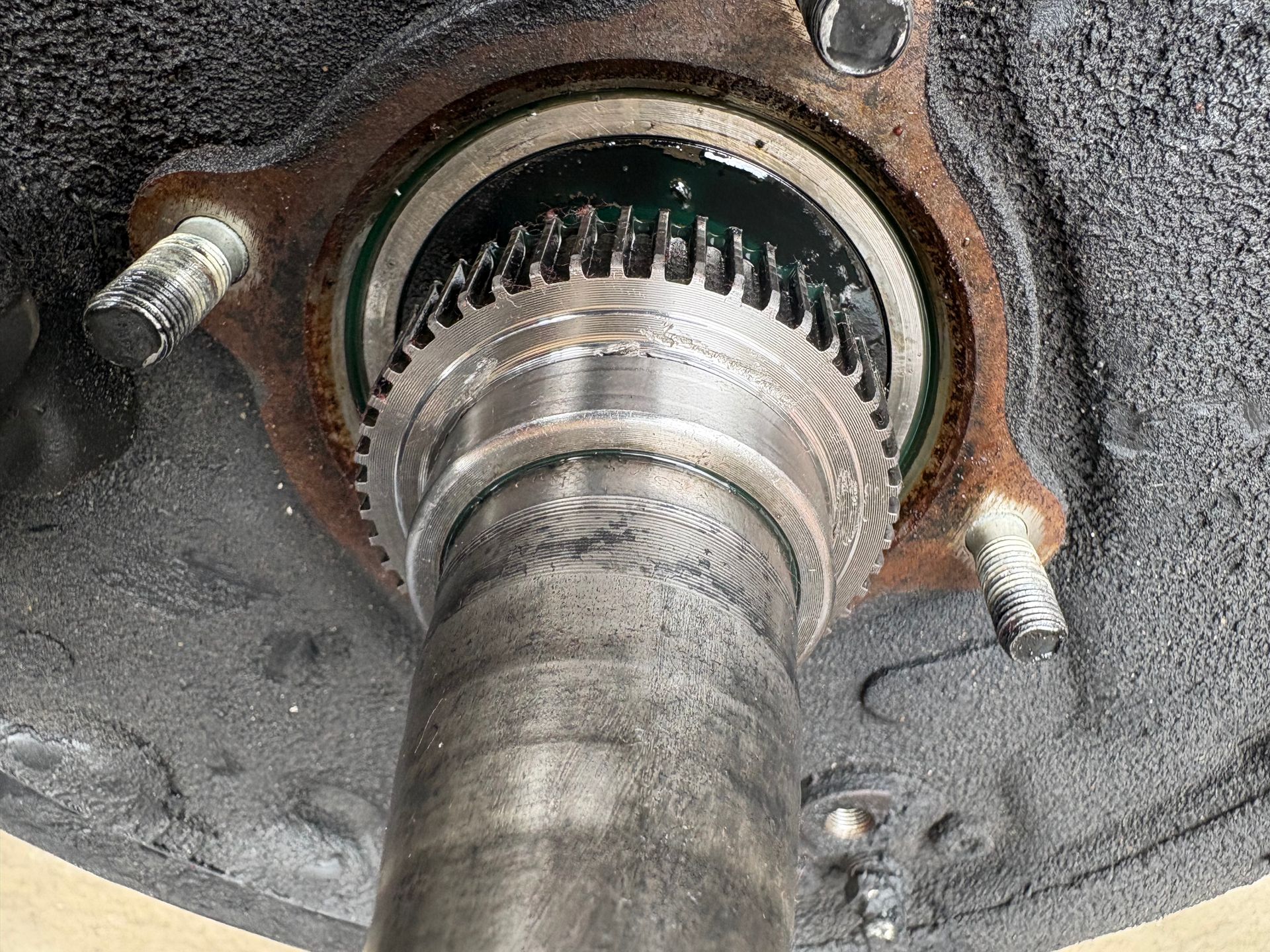 Close-up of a rusty metal axle hub with exposed splines and bolts mounted in a wheel well.
