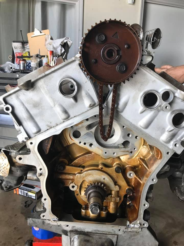 Disassembled car engine with timing chain and cam gears exposed in a workshop