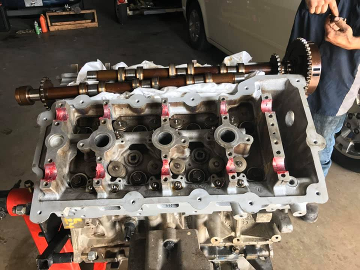 Engine cylinder head on a workbench in a garage, with a person standing beside it.