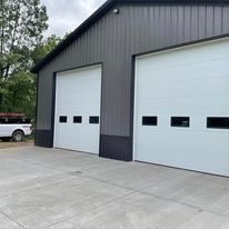 A gray metal commercial building with two white overhead doors featuring small windows at the bottom.