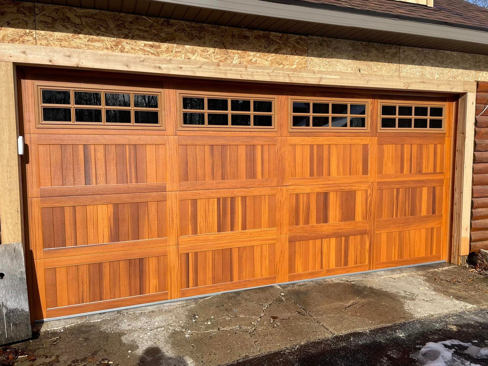A wide wooden garage door with a polished natural finish and a row of small windows across the top.