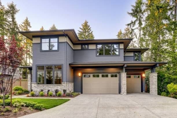 Front exterior of a modern two-story home with dark gray siding, tan accents, and two matching tan garage doors.