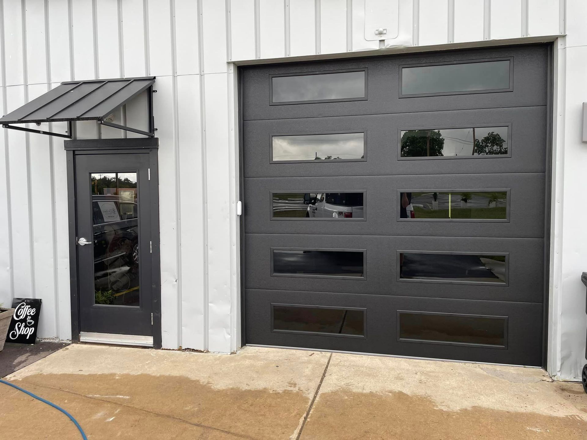 A black modern garage door with multiple rectangular glass window panels and a matching entry door with a small awning.