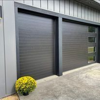 A dark gray corrugated metal building with two white commercial garage doors featuring small horizontal windows.