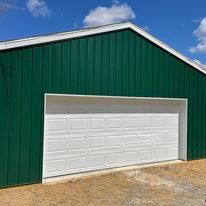 The upper gable of a dark green metal building with white trim and a white garage door.
