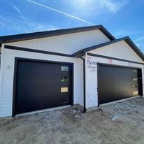 Three white carriage-style garage doors with windows and black hardware on a dark brick building.