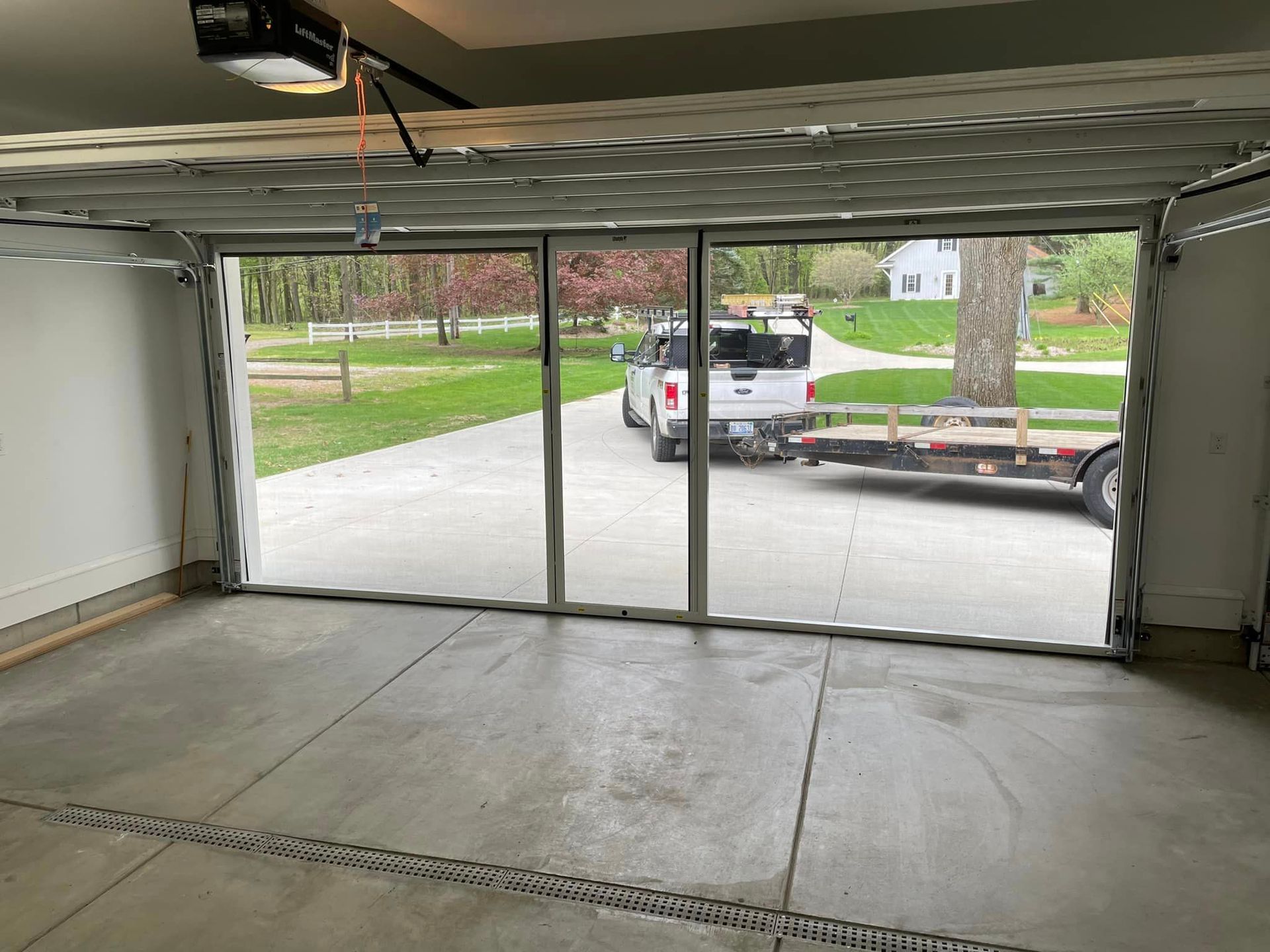 Interior view of a garage looking out through a sliding screen door at a truck and trailer parked on a concrete driveway.