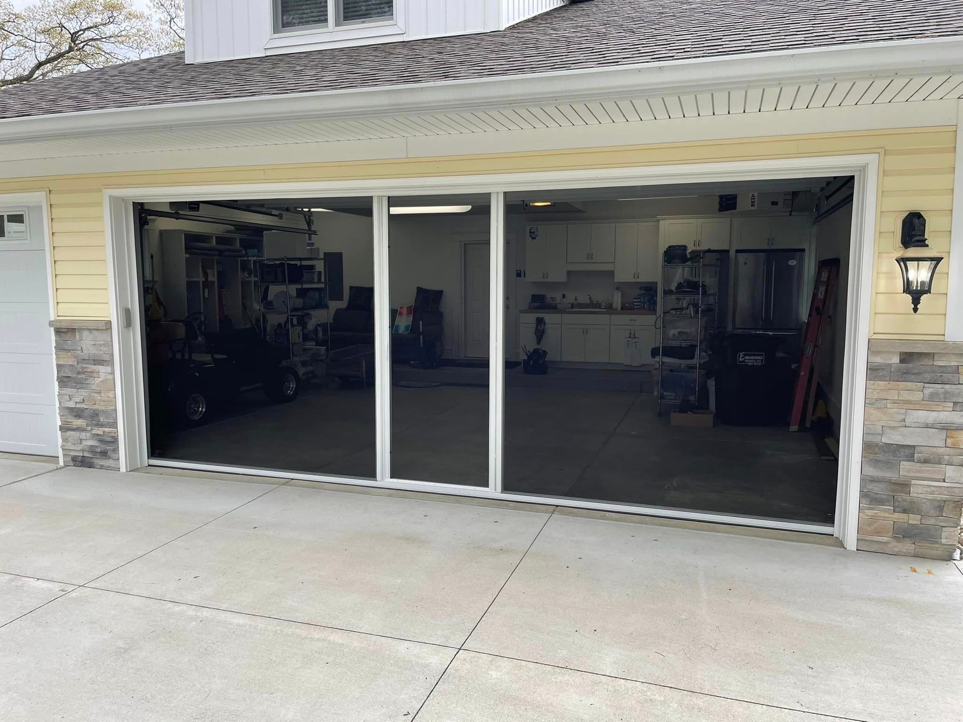 Exterior view of an open garage featuring a white-framed, three-panel sliding screen door system.