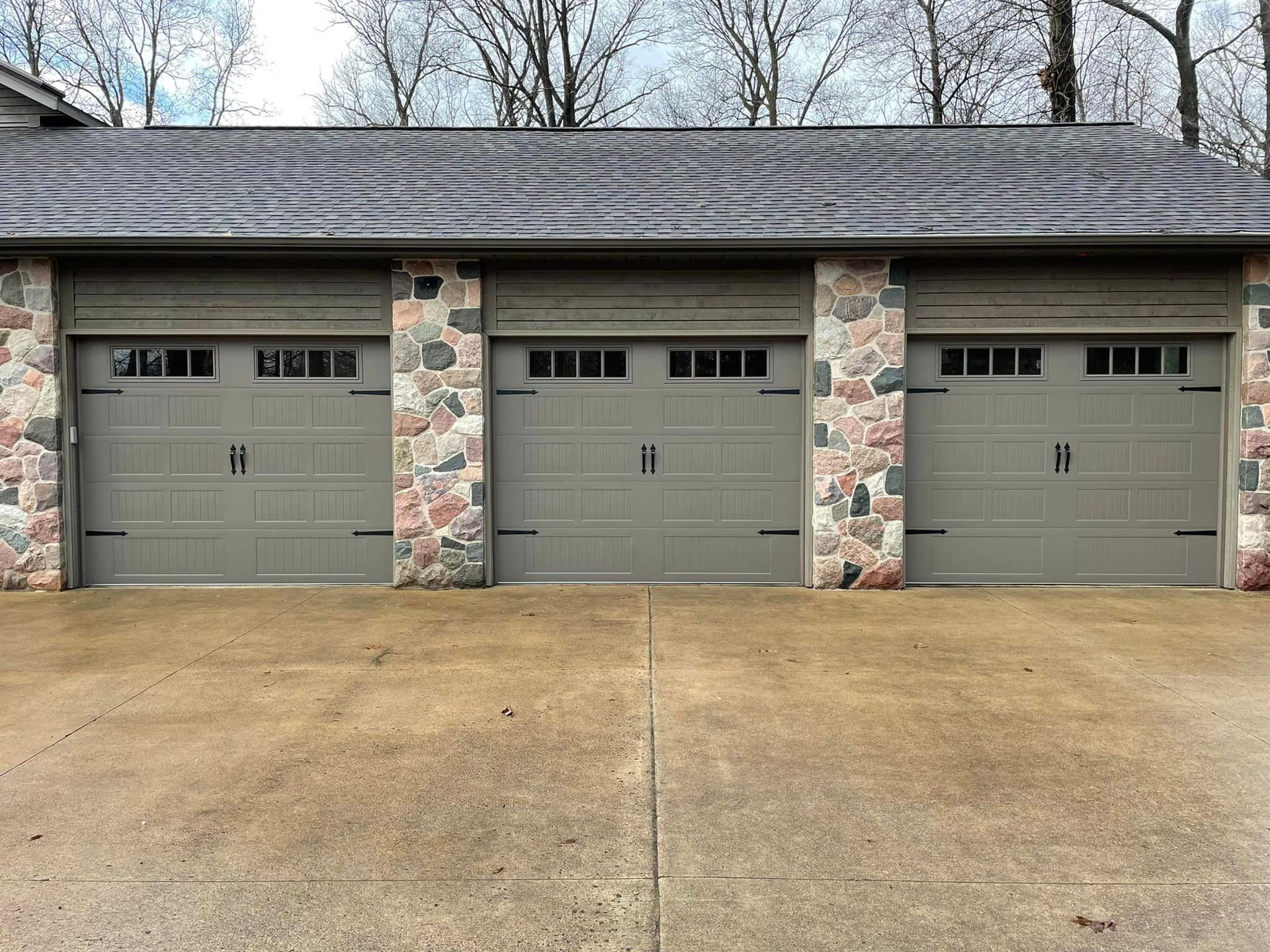 Three gray carriage-style garage doors installed on a stone-facade building.