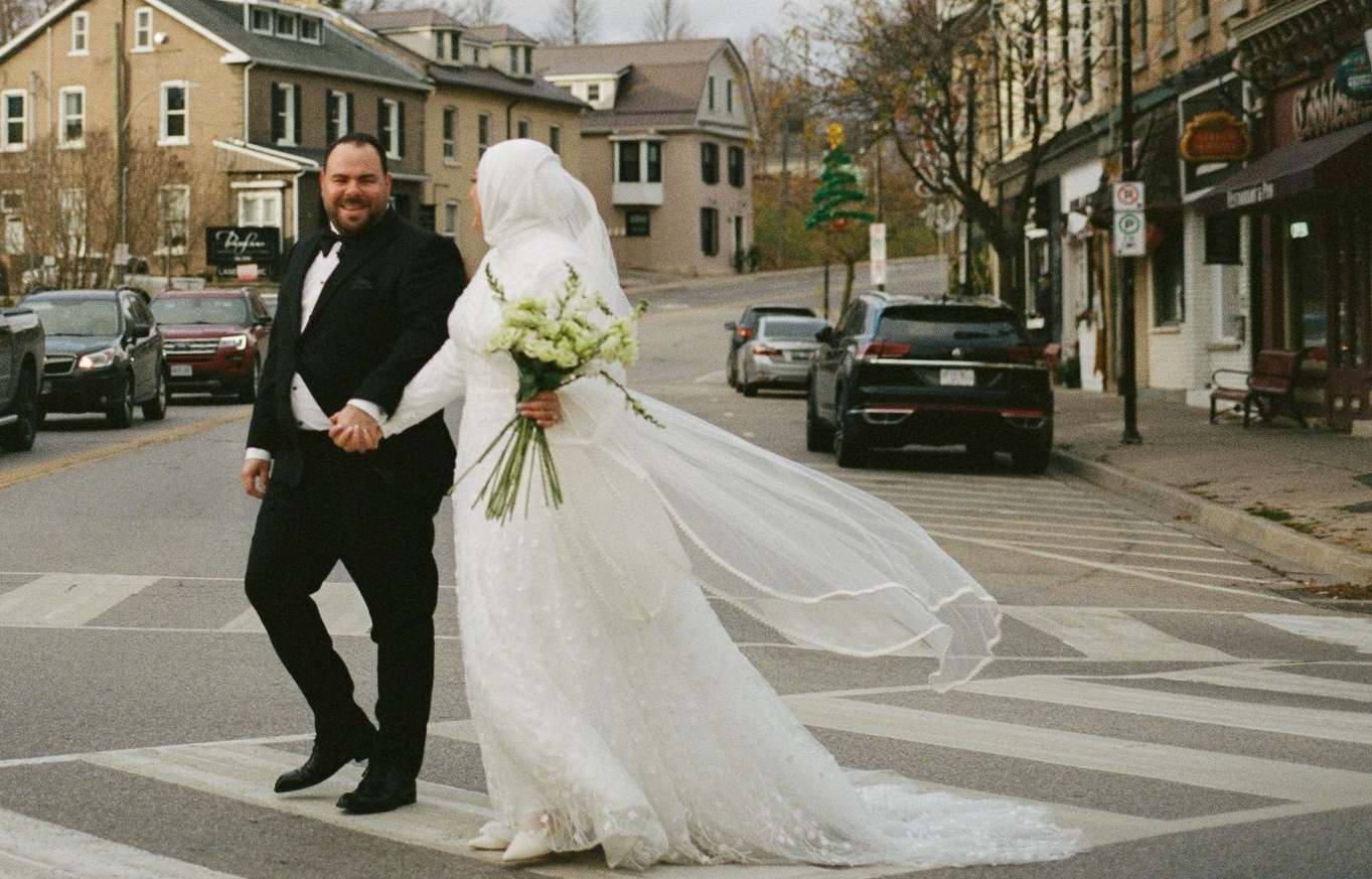 Real bride wearing a custom modest wedding gown with long sleeves and a flowing train from More 2 Lo