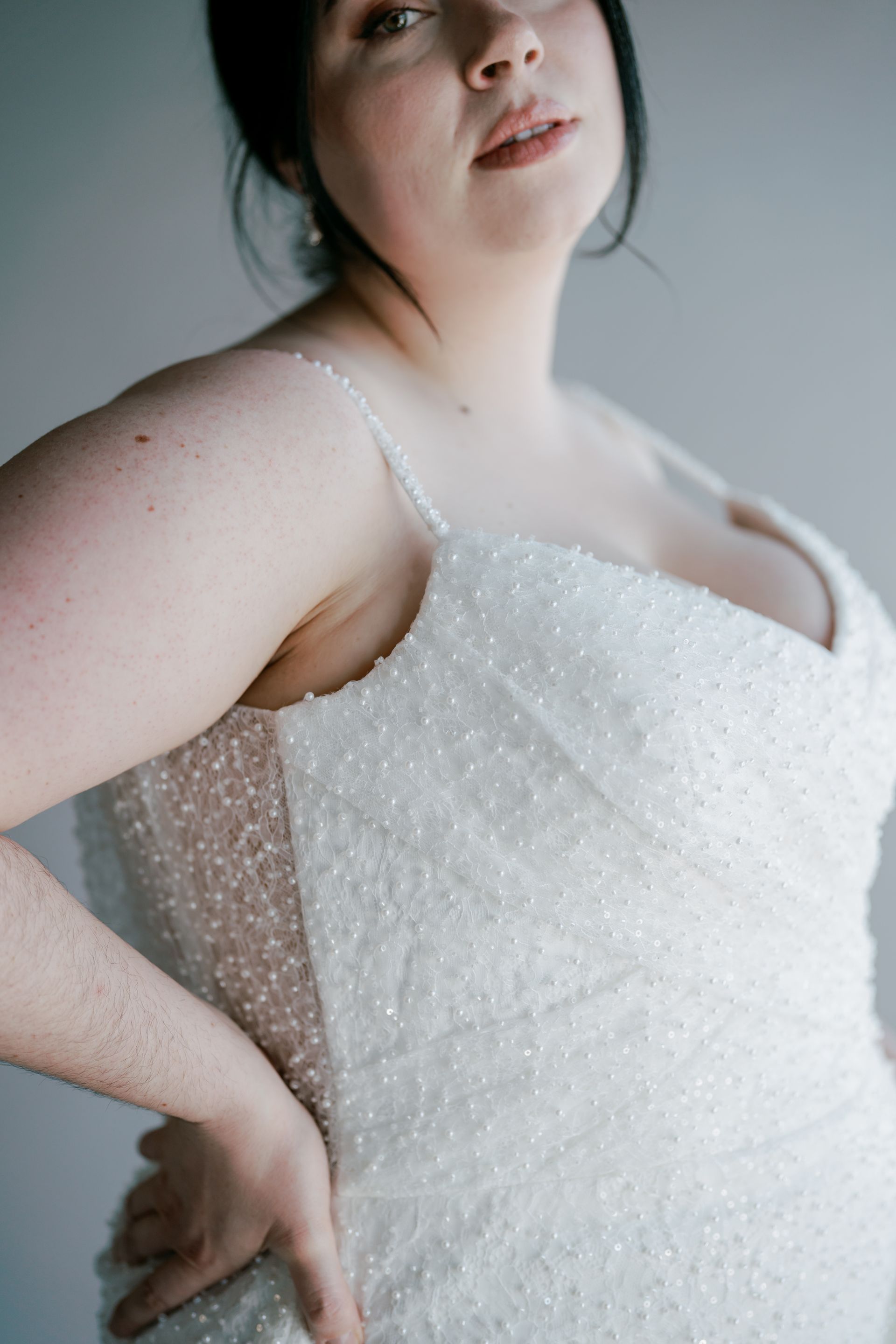 Woman in sparkly white wedding dress, hand on hip, looking up.